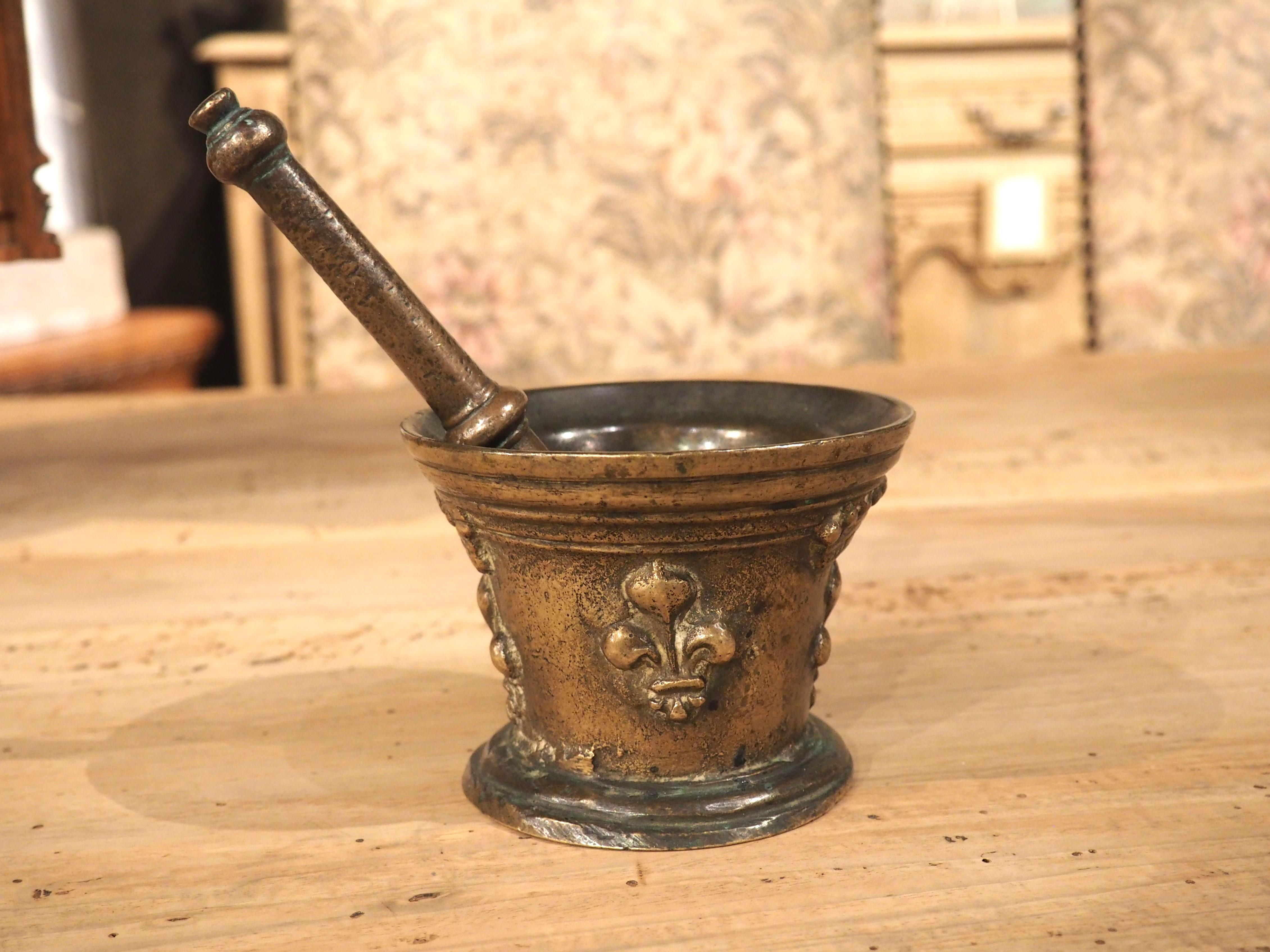 This small bronze mortar and pestle are from France, circa 1700. The circular opening has several layers of molding, with the bottom three interrupted by a pair of open crowns on opposing sides. Both crowns have a fleur de lys beneath it, with two