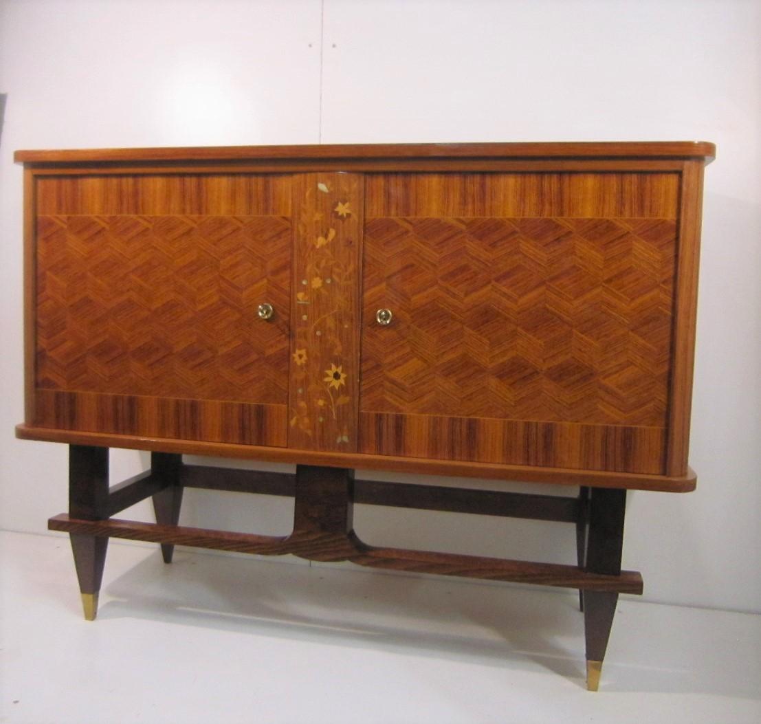 A French Modern parquetry and marquetry inlaid two-door buffet raised on sculptural plinth with tall tapered legs ending in brass sabots .
Exotic wood and mop Inlaid imagery of birds and squirrels on branches grace the central panel. The two doors