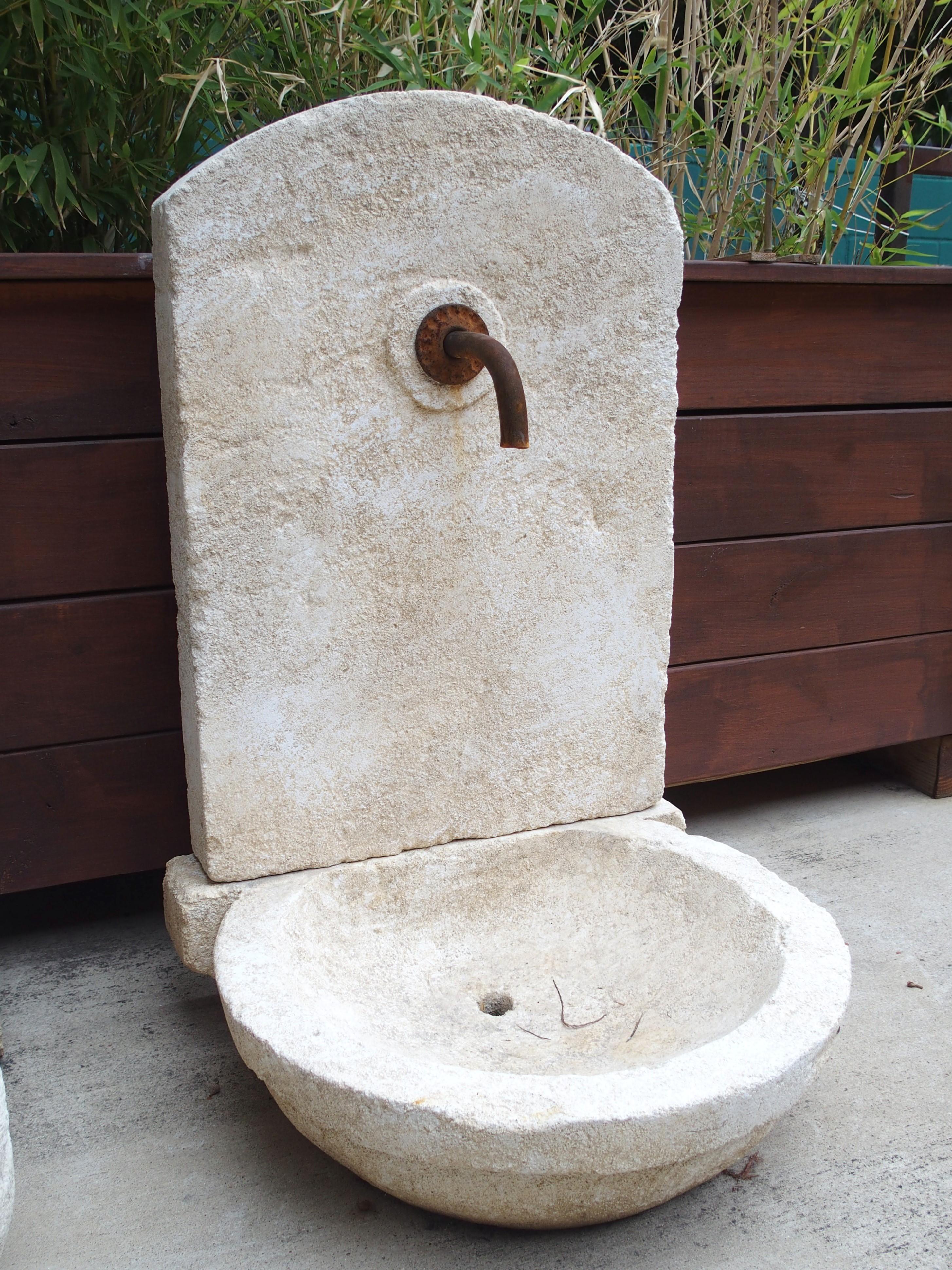 This small wall fountain from Provence, France, has been hand-carved in two sections from Estaillade limestone. The back of the round basin was carved with a thick horizontal ridge, which functions as a support for the arched back wall. An iron