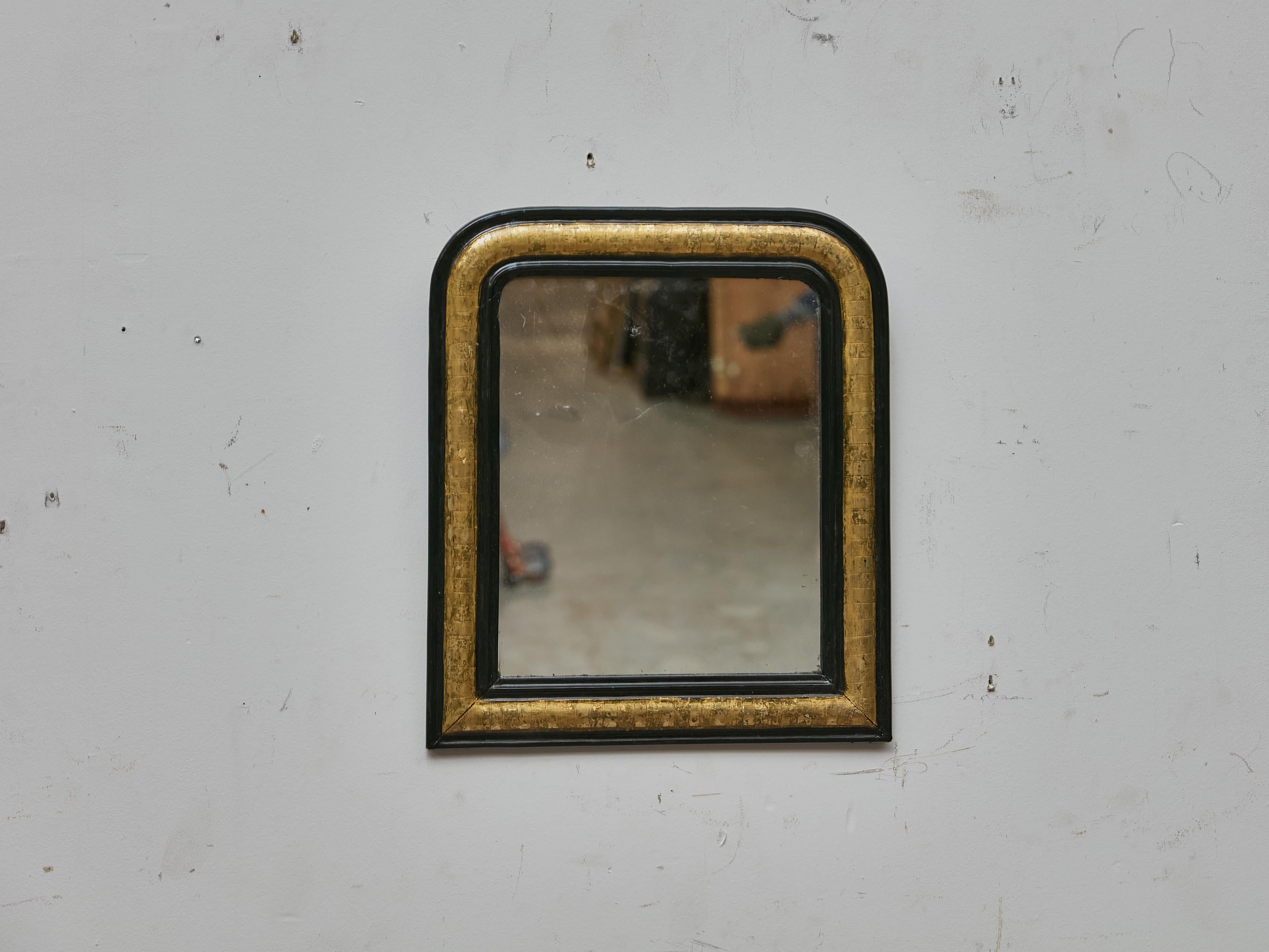 A charming mid-19th century French Louis-Philippe mirror, distinguished by its compact proportions and refined use of contrast. The frame features the classic Louis-Philippe shape, with rounded upper corners and a subtly angled lower profile,