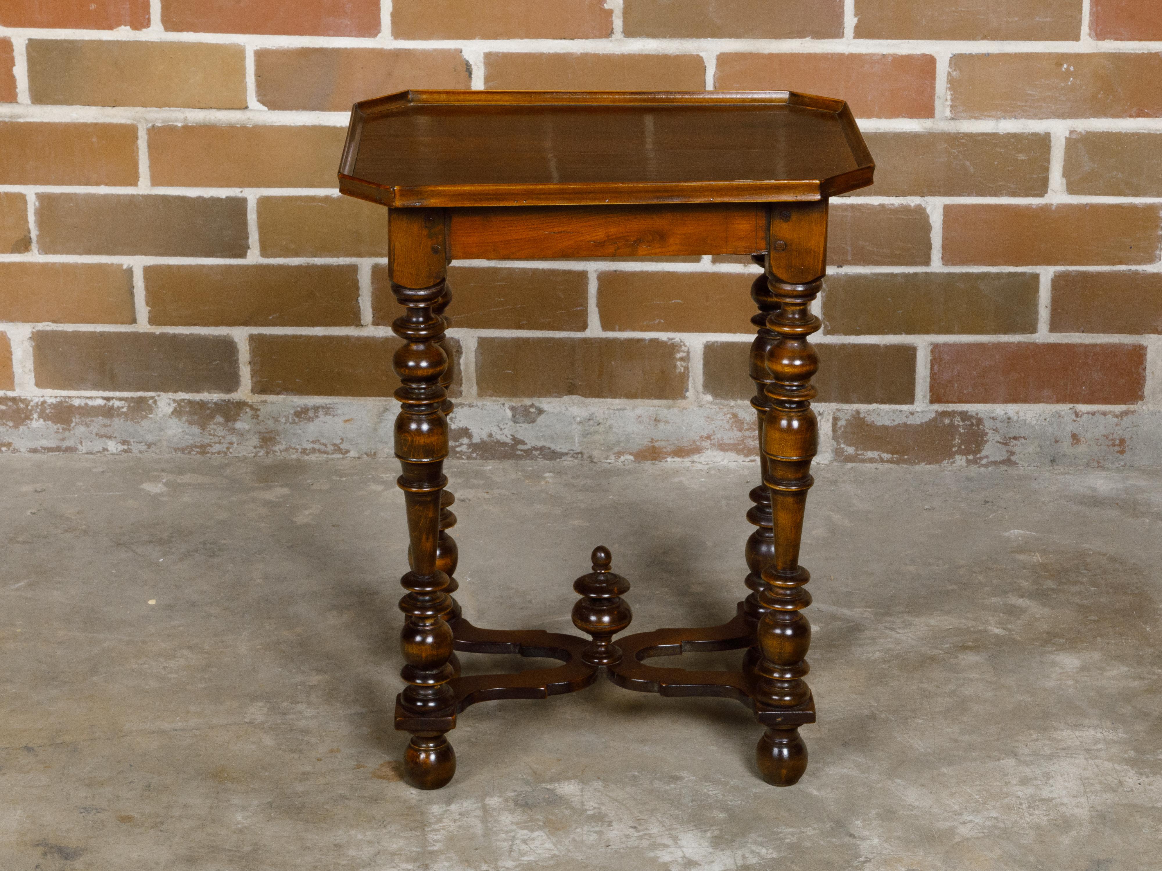 A petite French Louis XIII style walnut side table from the 19th century with tray top, spool legs and carved X-Form cross stretcher. This charming petite French Louis XIII style walnut side table, dating back to the 19th century, captures the
