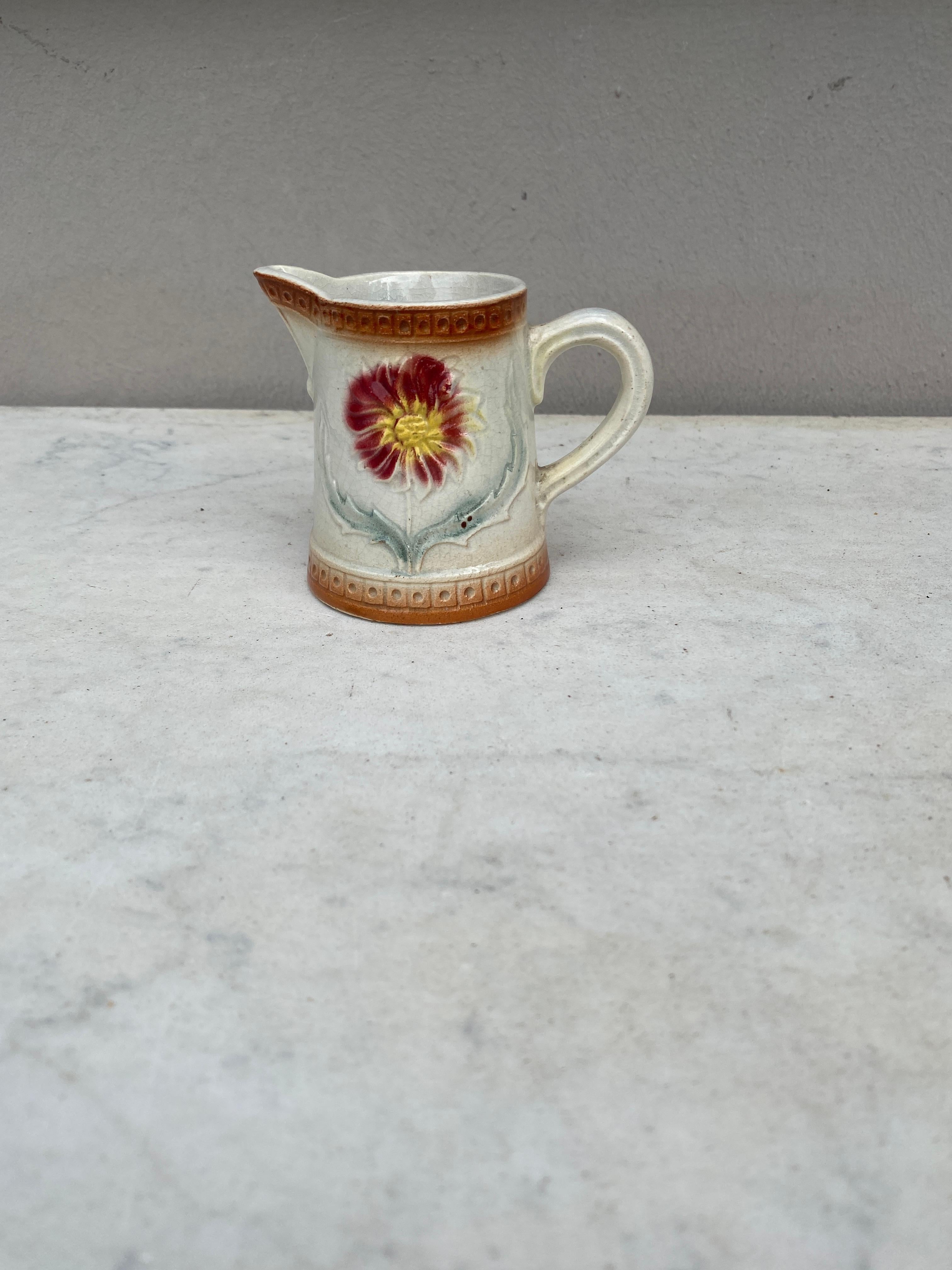 Charmant petit pichet crémier en majolique française décoré d'une fleur rouge.