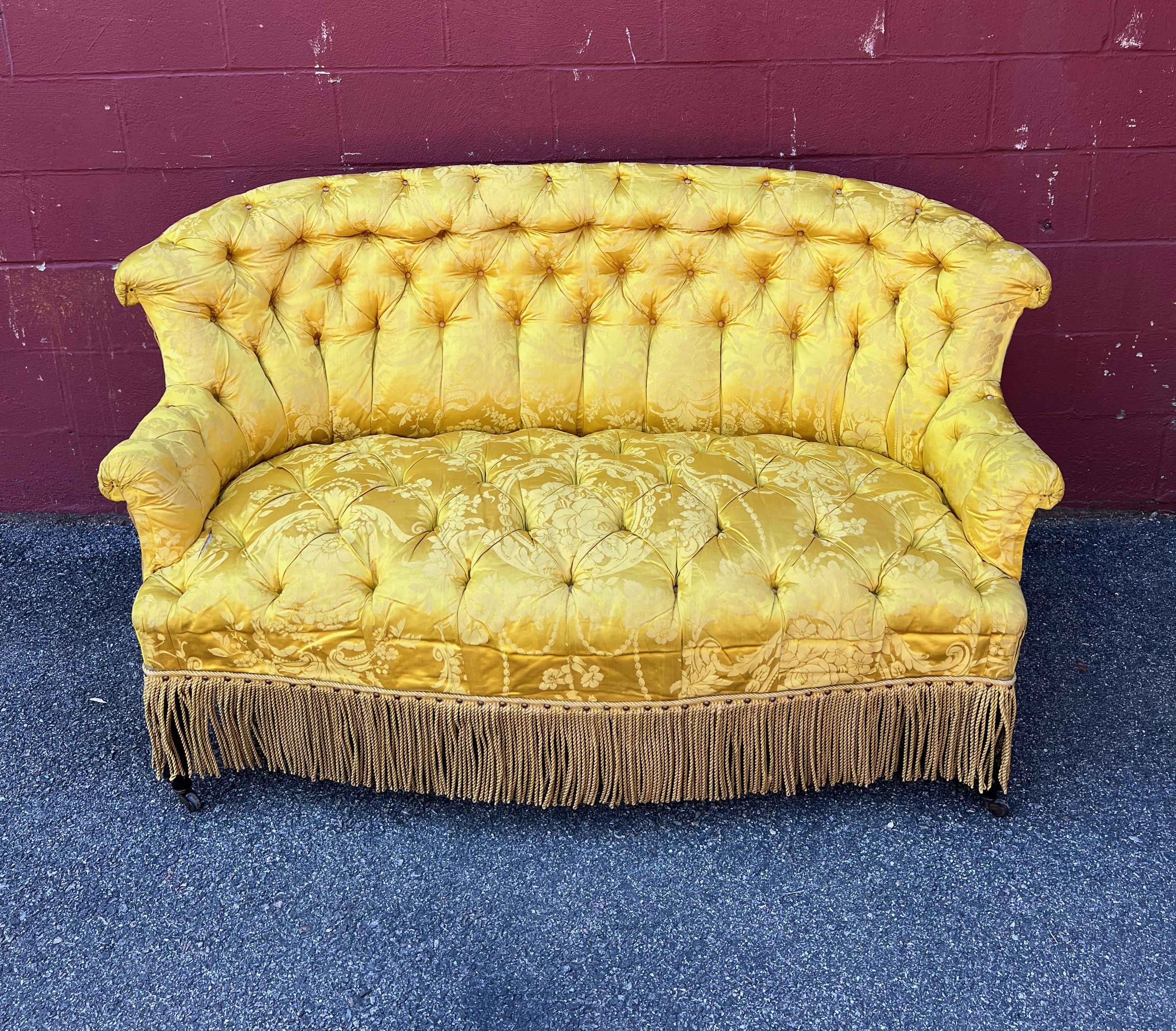 An  exquisitely tufted small sofa or settee with graceful rolled arms and back. Both the back and seat are tufted in a yellow/ gold damask silk and the back is upholstered in a contrasting solid fabric. The sofa is finished off in a matching