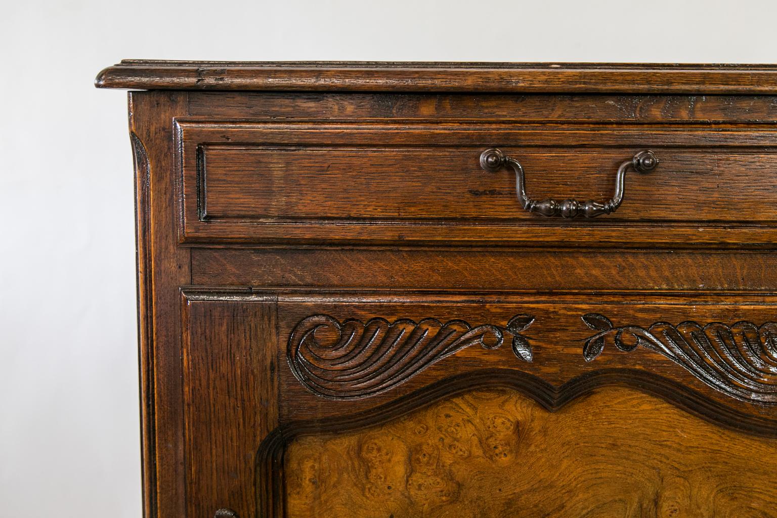 The top of this small French oak buffet has heavy bullnose molding. The top of the door has a shaped carved design. The molded door frame surrounds a recessed burl wood panel. The door has the original working lock and key. The corners have convex,