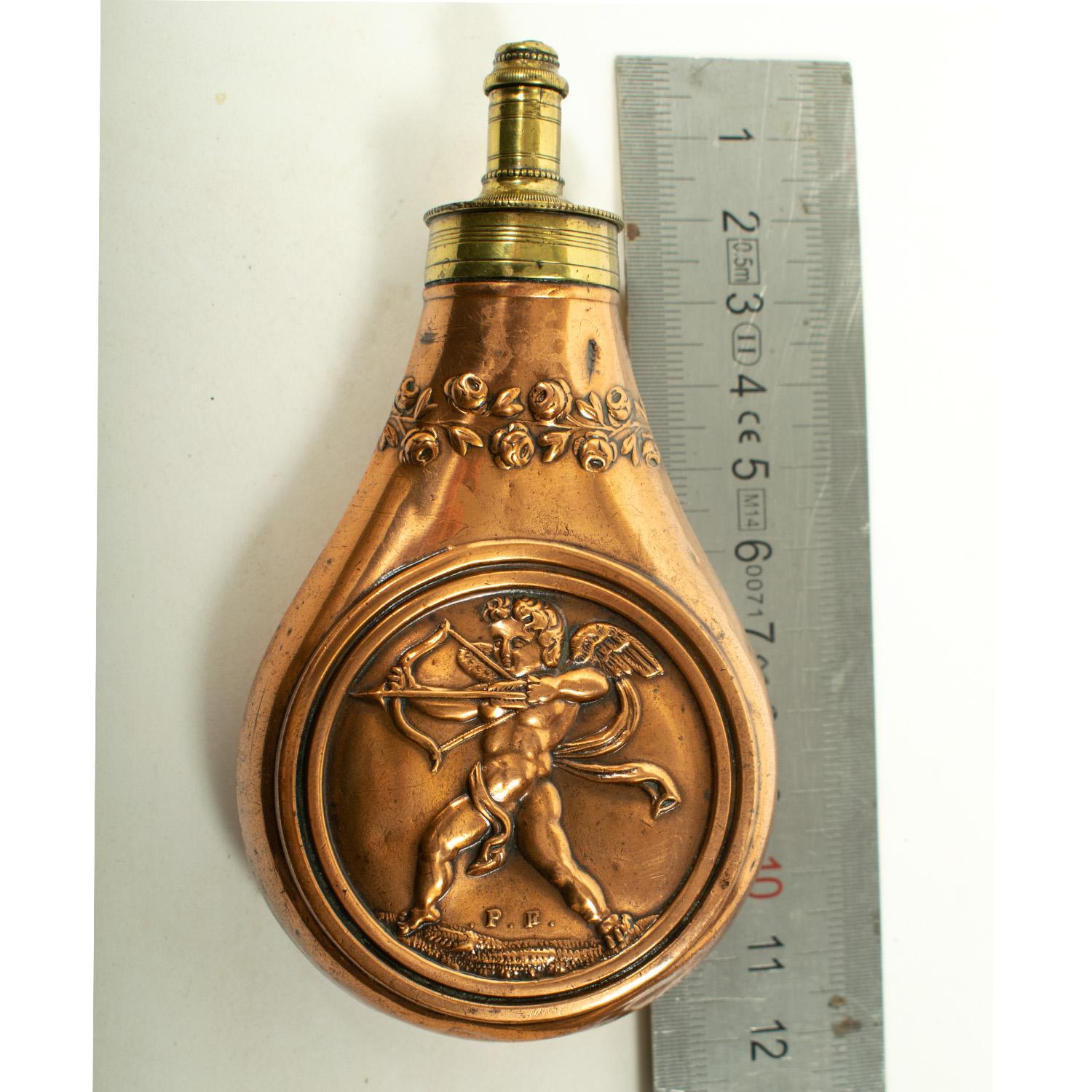 PETITE FLASQUE PISTOLET FRANÇAISE, 19E SIÈCLE

Une gourde en laiton et en cuivre finement ouvragée, mesurant 11,5 cm hors tout, présentant un motif fortement estampé d'un Cupidon avec un arc et une flèche dans un cercle et garni d'un anneau de roses