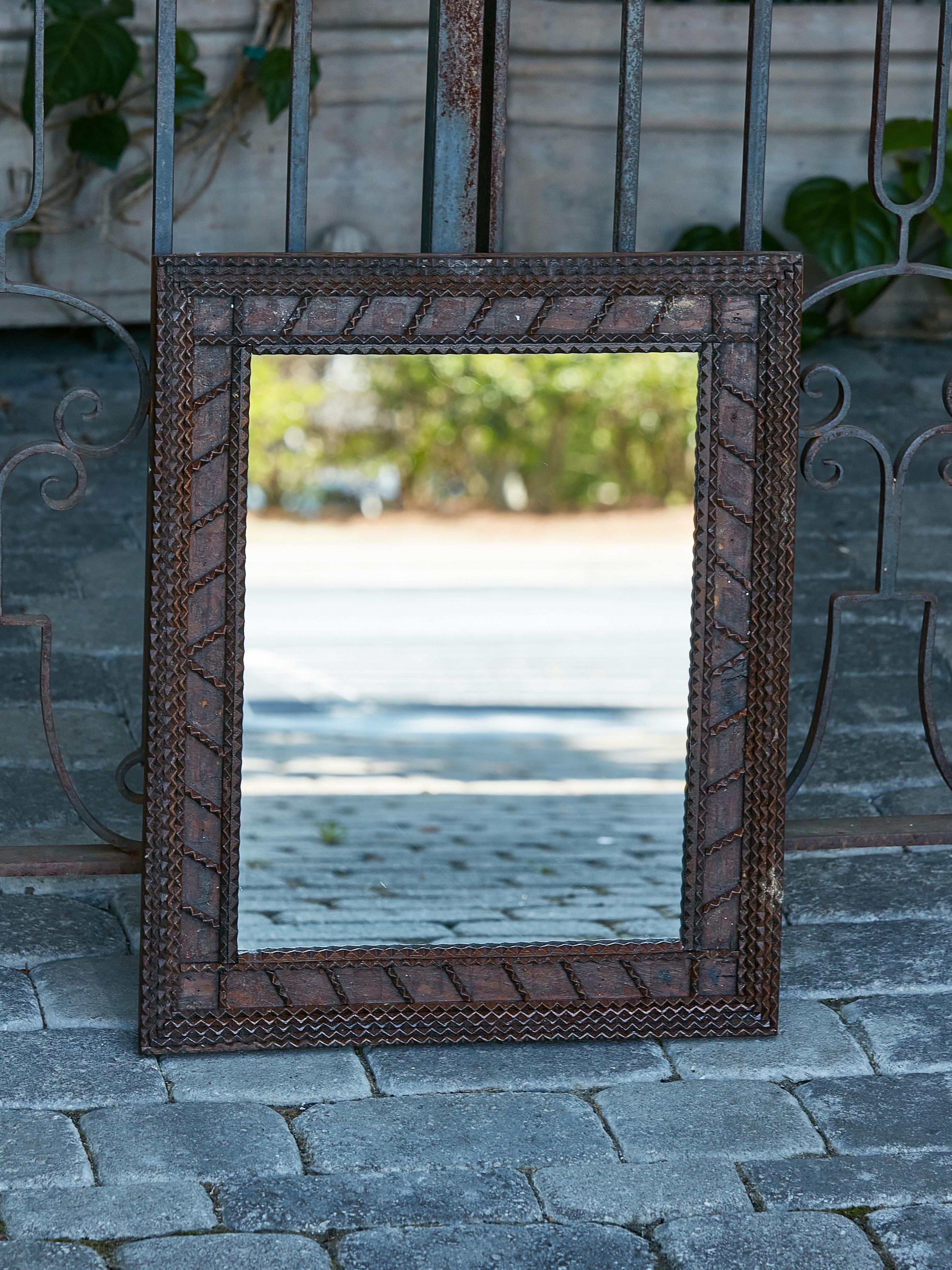 A small French Tramp Art Turn of the Century mirror from circa 1900 with wavy patterns and dark brown patina. An alluring melange of artistry and timeworn charm, this small French Tramp Art mirror from the Turn of the Century, circa 1900, is a