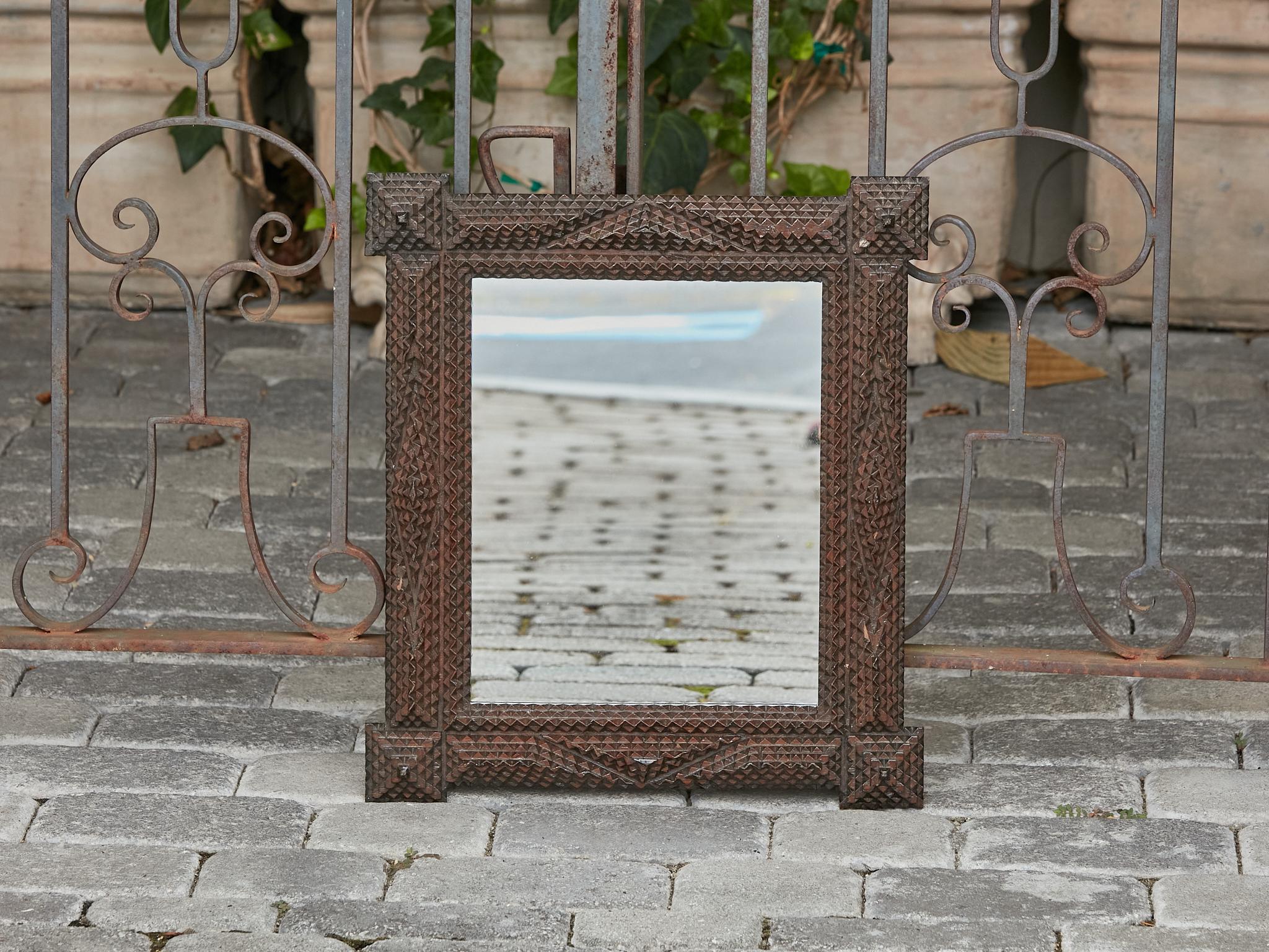 A small French Tramp Art hand-carved wooden mirror from the Turn of the Century circa 1900 with raised pyramidal motifs and dark brown patina. Embrace the rustic elegance of this charming French Tramp Art hand-carved wooden mirror from the Turn of