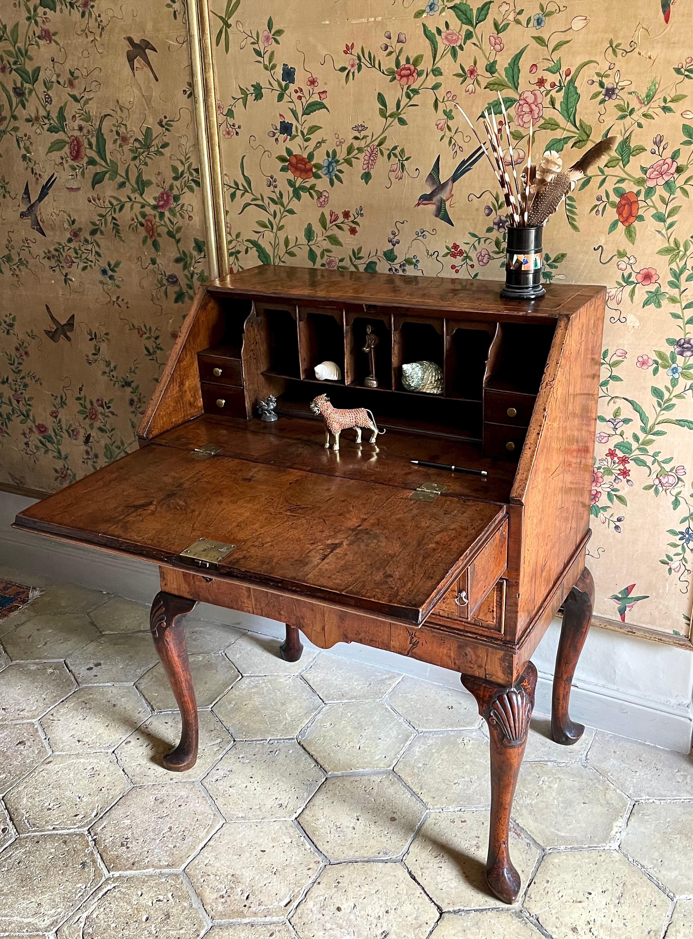 George I period walnut bureau or desk on stand, of compact proportions, ca 1720.

This small early Georgian desk is veneered in walnut and, unusually, is banded in yew wood. The well-drawn cabriole supports are carved with shells, a further