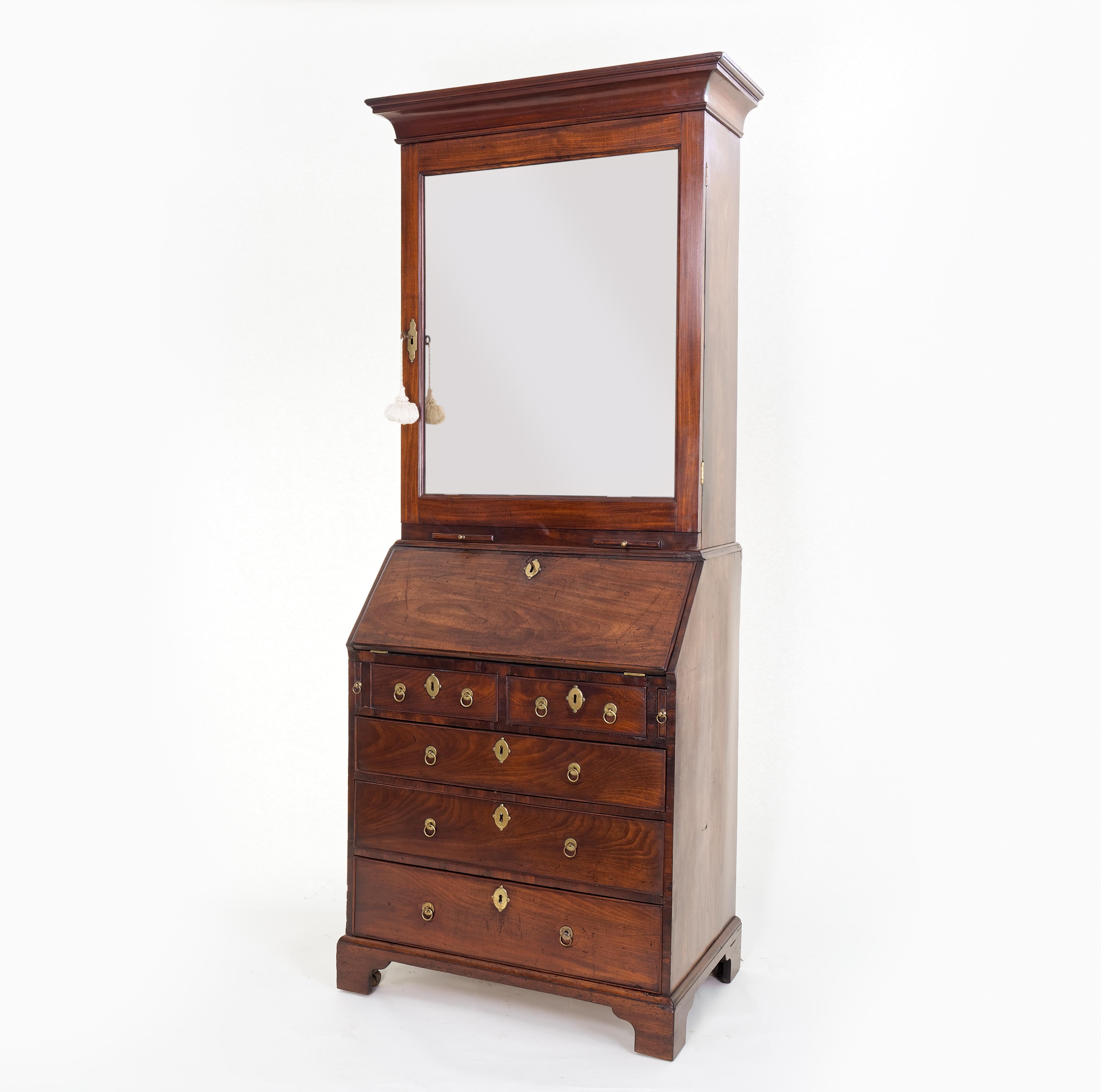A fine and rare George II/Early George III mahogany bureau bookcase of rare small size, (often referred to as a ‘Lady’s Bureau’). The top half with cavetto cornice above a mirrored door which encloses bookshelves and the lower half with fall-flap