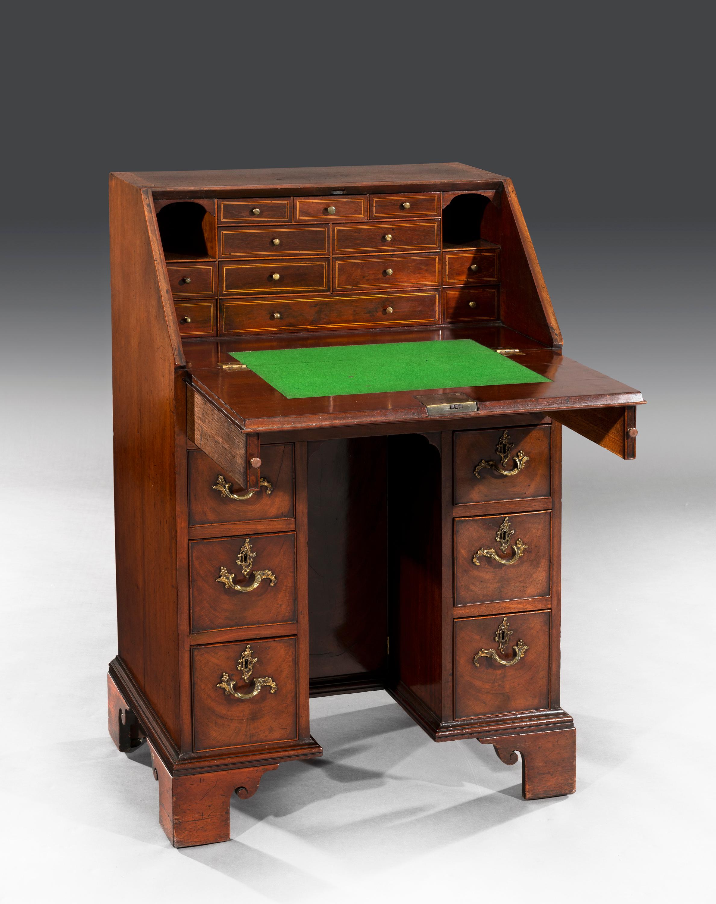 The faded mahogany fall opens to reveal a bank of inlaid drawers flanked by pigeon holes above a baized writing surface. The flamed mahogany kneehole bureau is arranged with one long and six short oak lined drawers which retain brass Rococo handles