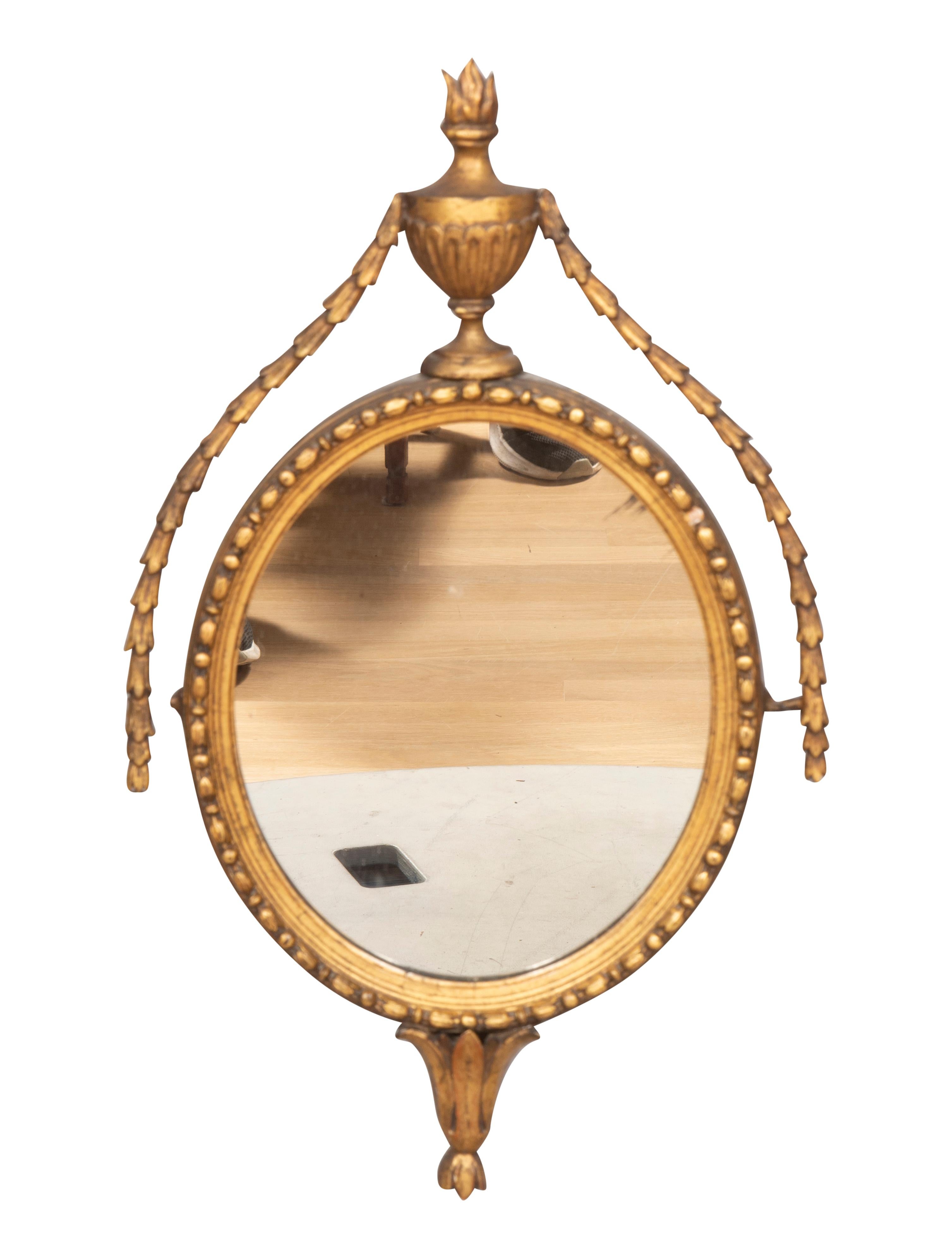 With urn finial and bellflower swags over an oval mirror and conforming carved frame ending with a leaf tip cluster.