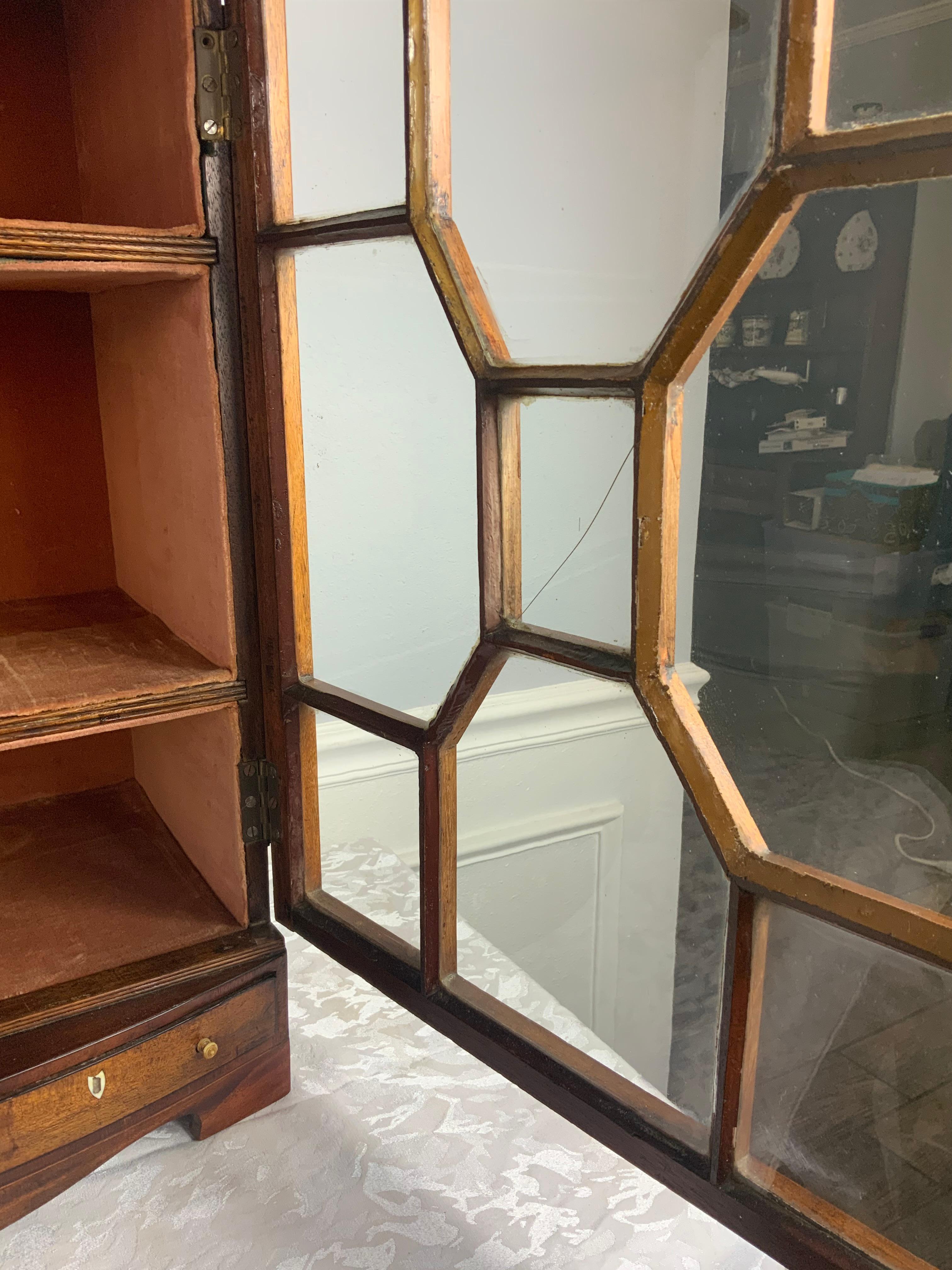 An attractive small size Georgian Mahogany display cabinet with fixed shelves and a fitted fabric interior.  Decorative molded sides that match the moldings on the exterior of the door.  Individual glazed glass door panels with the original wavy