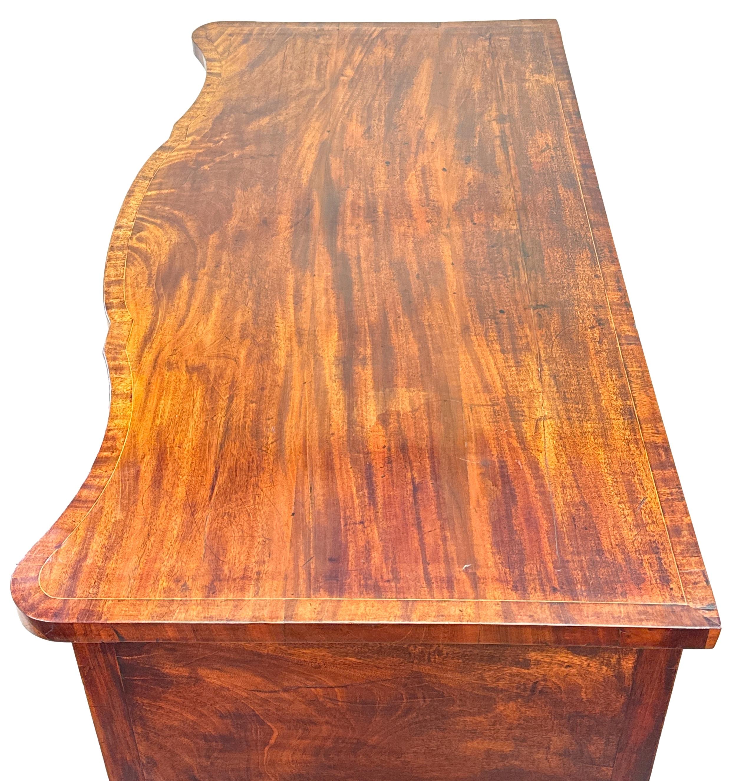 

Una credenza a serpentina in mogano del tardo XVIII secolo, periodo Giorgio III, di piccole e rare proporzioni, estremamente attraente e di ottima qualità, con un piano superbamente strutturato e incorniciato, quattro cassetti che conservano le