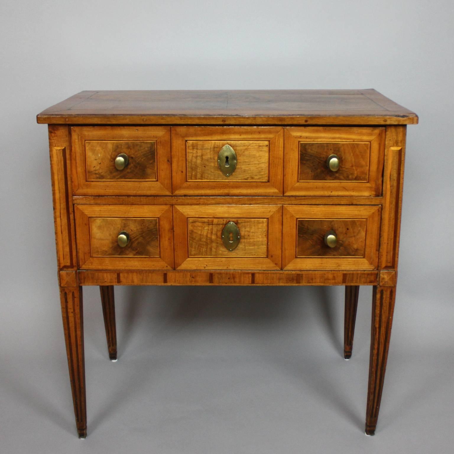 A small German Neoclassical marquetry commode with a rectangular top above two drawers each with three walnut panels and fine banding. With corresponding marquetry on sides and top, on square tapering legs. With brass mounts and a beautifully