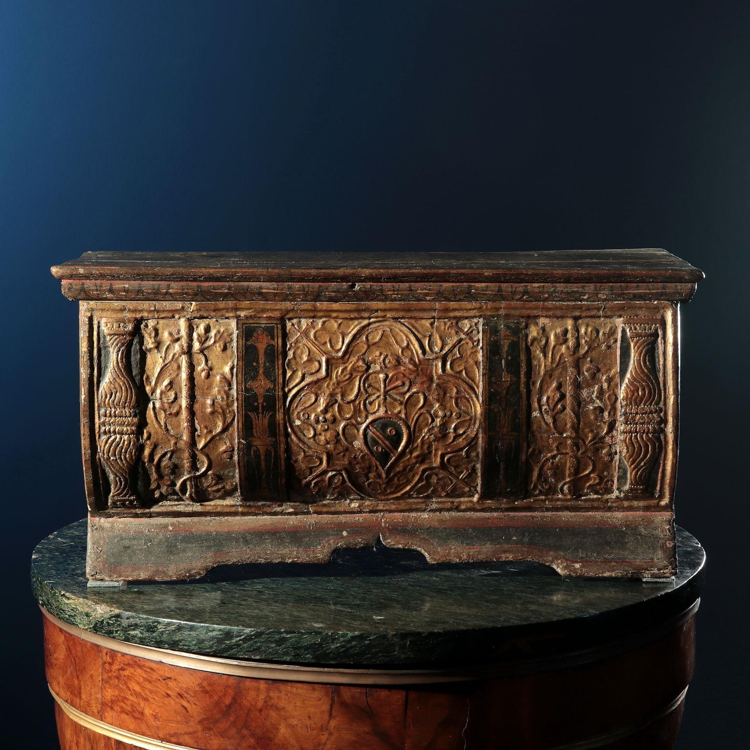Pequeña caja con abertura superior, frente de urna ligeramente convexo con soporte de repisa perfilada, decorada en el frente con tablilla tallada, mientras que el resto del objeto está simplemente pintado. La fachada comenzaba con cuatro pilastras