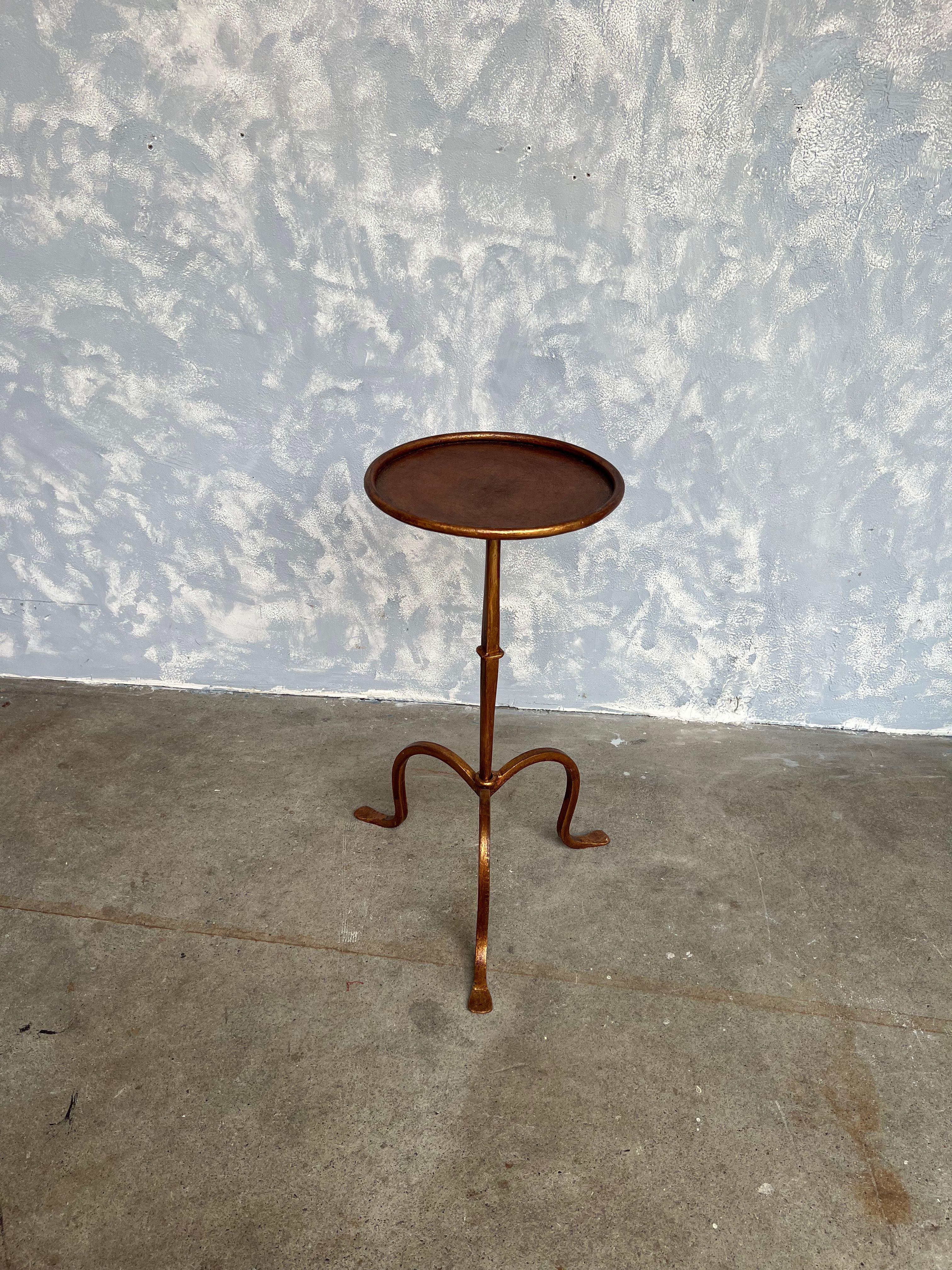 An elegant gilt iron drinks table on a tripod base with a central ring detail on the stem. The original finish is a hand applied gold patina with red undertones. These tables are wonderfully adaptable as they can be moved around as needed for an
