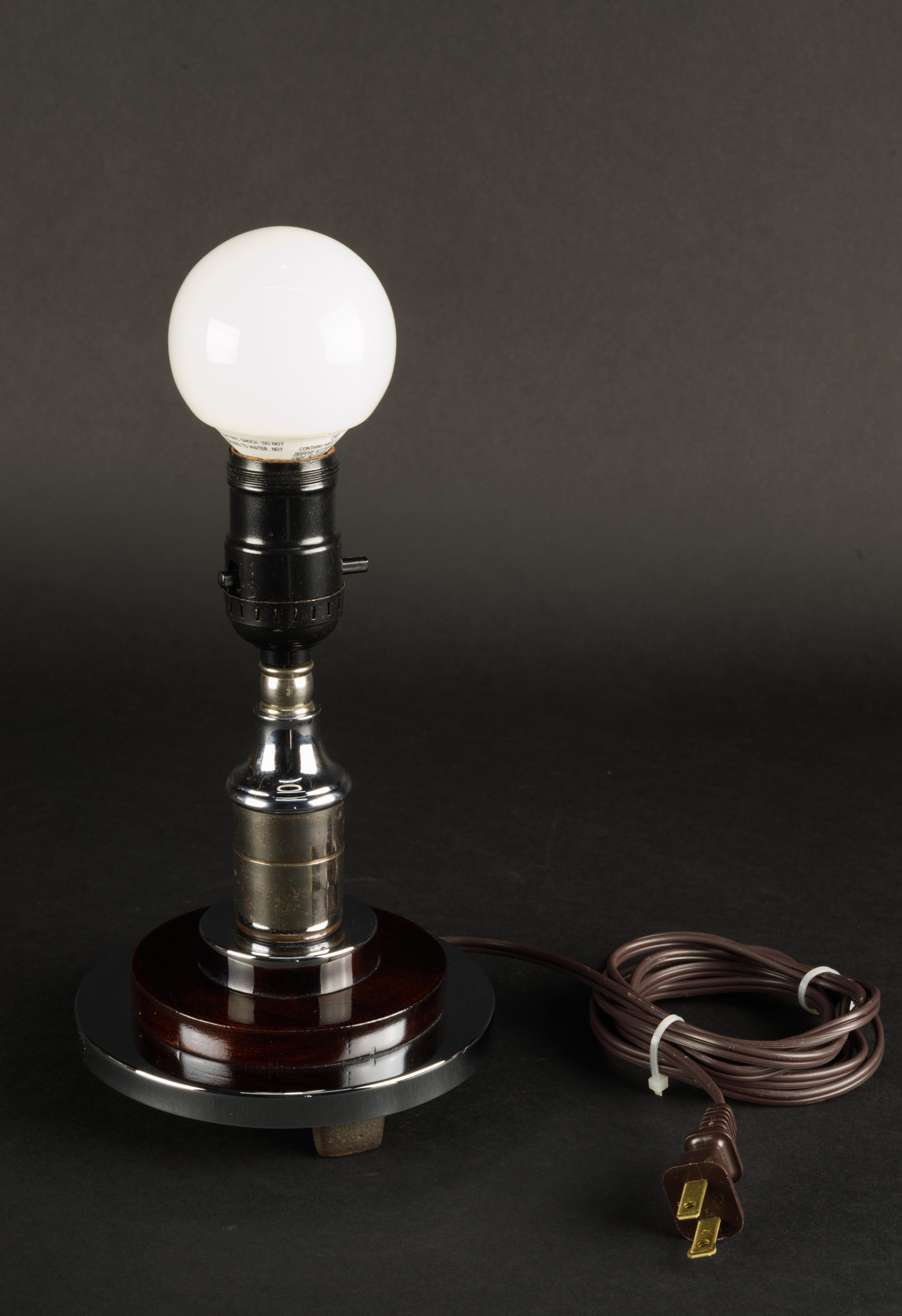 Small cute deco style table lamp in chrome. Wood spacer is lacquered and polished walnut. Therese some  deterioration to chrome. It's consistent with the age. Walnut lacquer looks good. Wire has been updated. E-26 socket with on/off push switch.