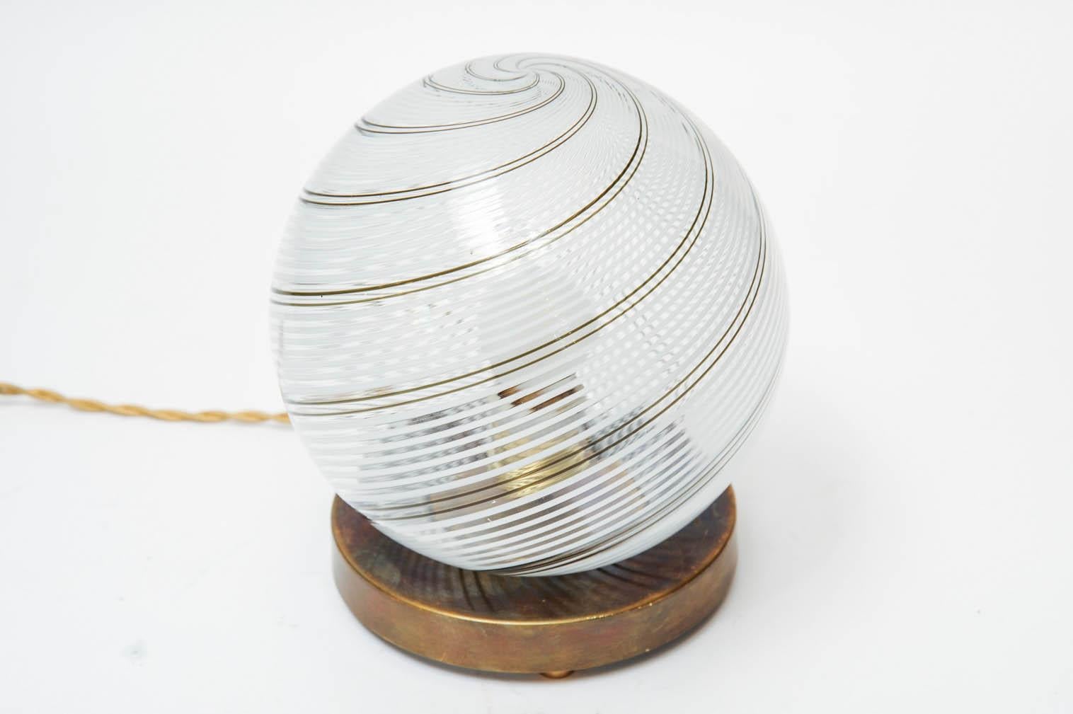 Table lamp made of a patinated brass circular foot with original stamp, topped with a small Murano glass globes with the typical Venini swirl stripes.