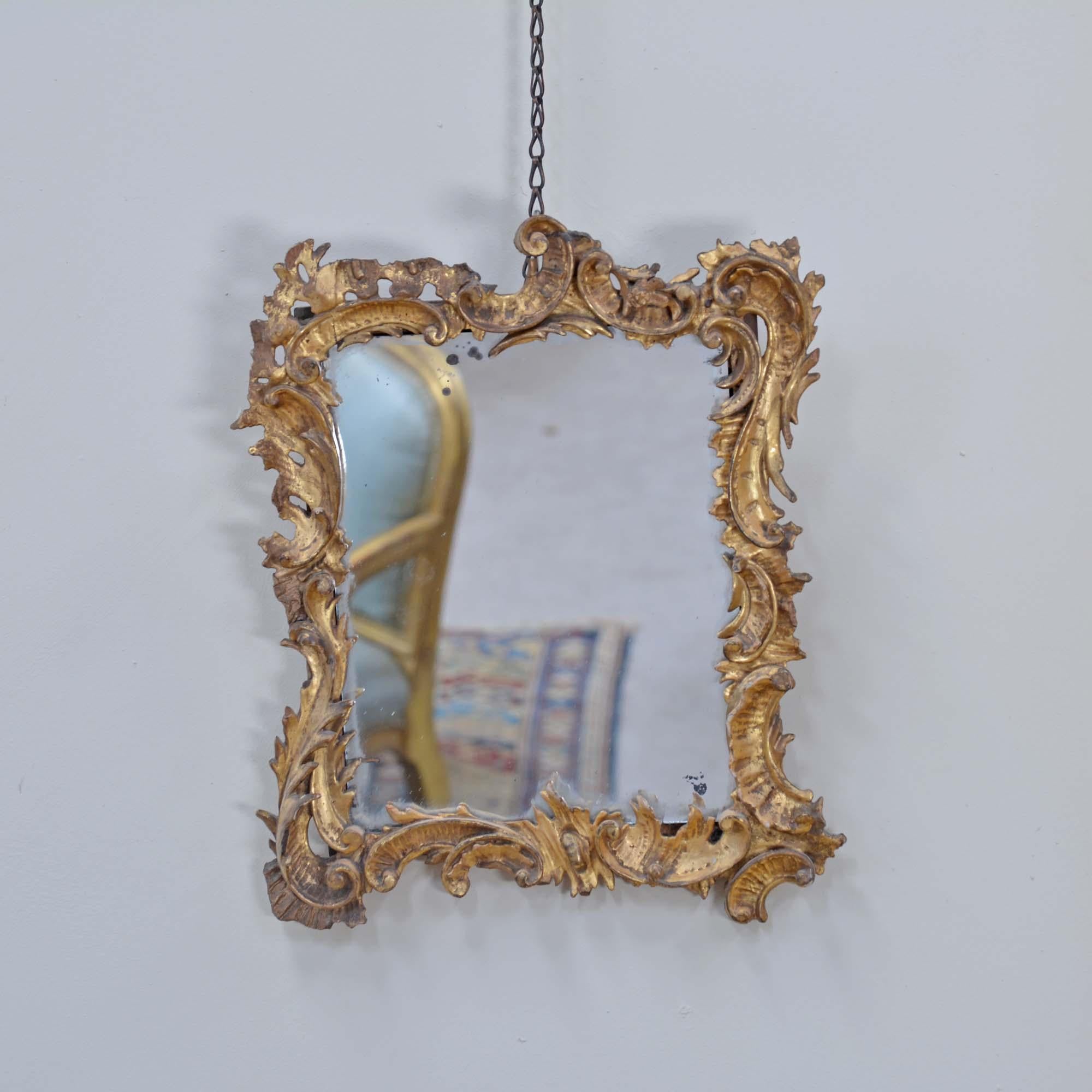 A small Georgian carved giltwood mirror with an asymmetrical carved wood foliate frame with C-scrolls in original water gilding. The mirror plate is later but with some character.
English, circa 1780

This mirror is carved wood rather than gesso