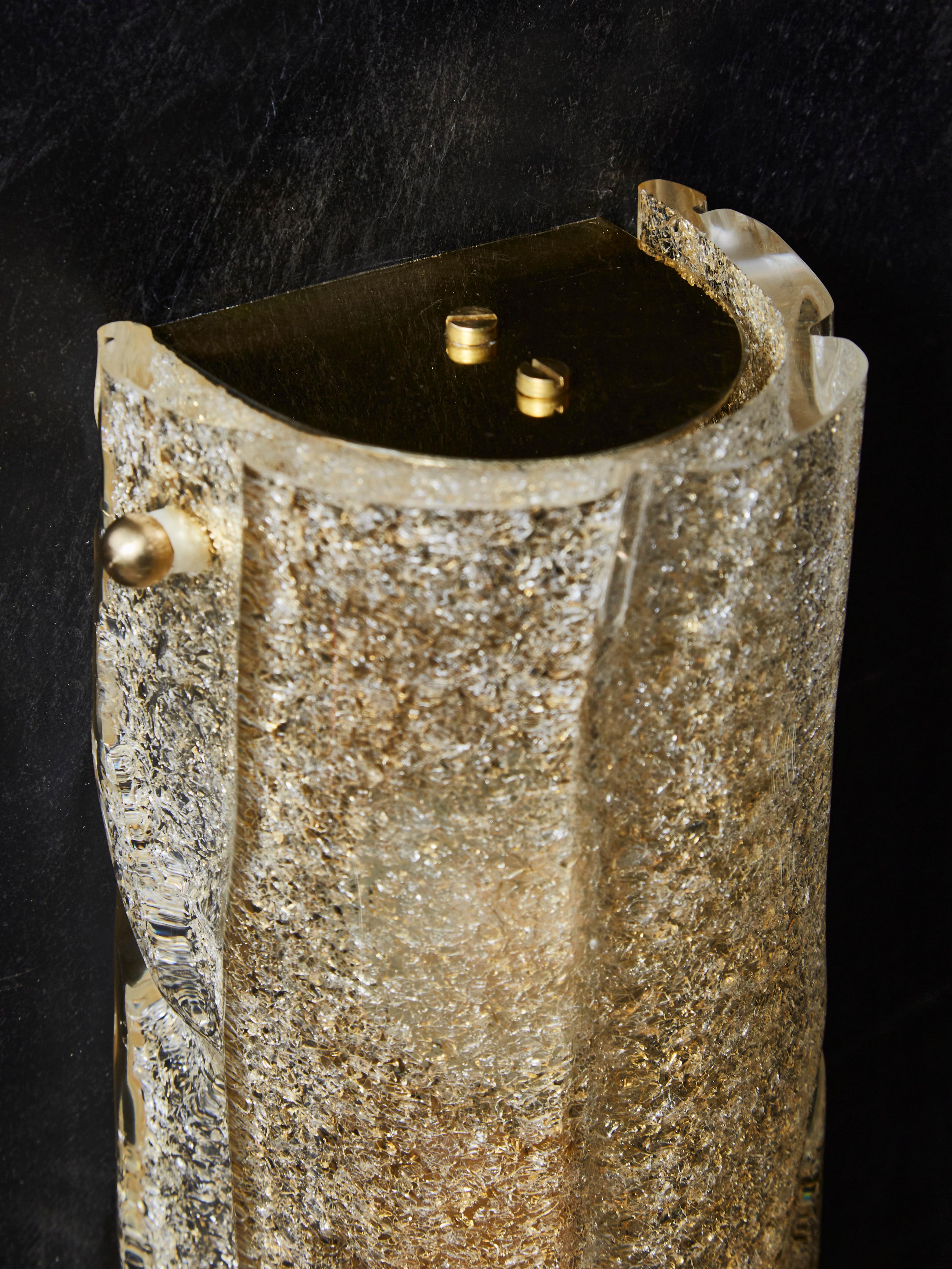 Small wall sconces made of a single piece of Murano glass, textured in gold color. Brass plates at the top and bottom.