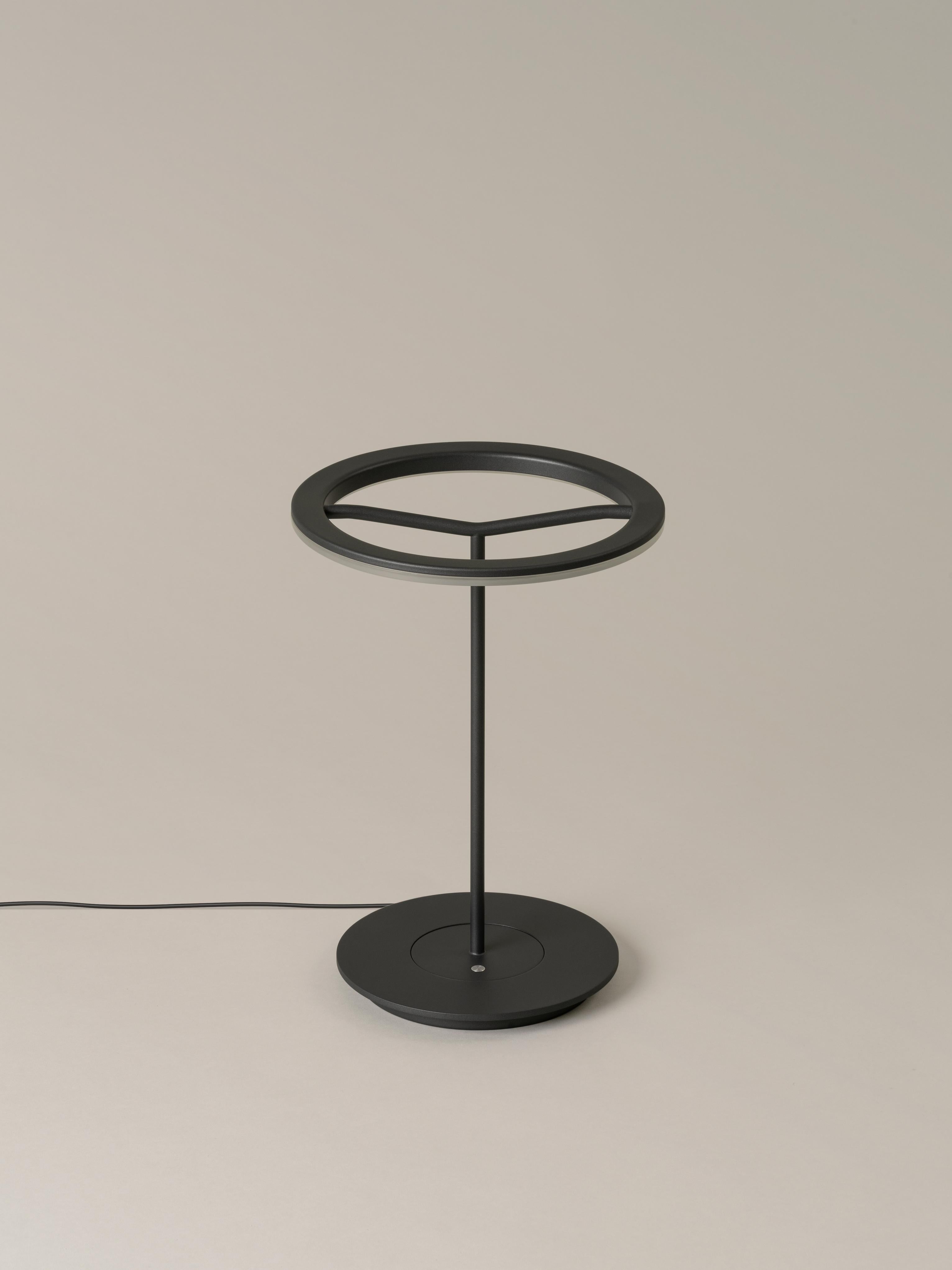 Small graphite sin table lamp by Antoni Arola
Dimensions: D 25 x H 36 cm.
Materials: Metal.
Available in white or graphite, with or without shade.

A lamp that combines simplicity and technology to create a lucent ring of light suspended in the