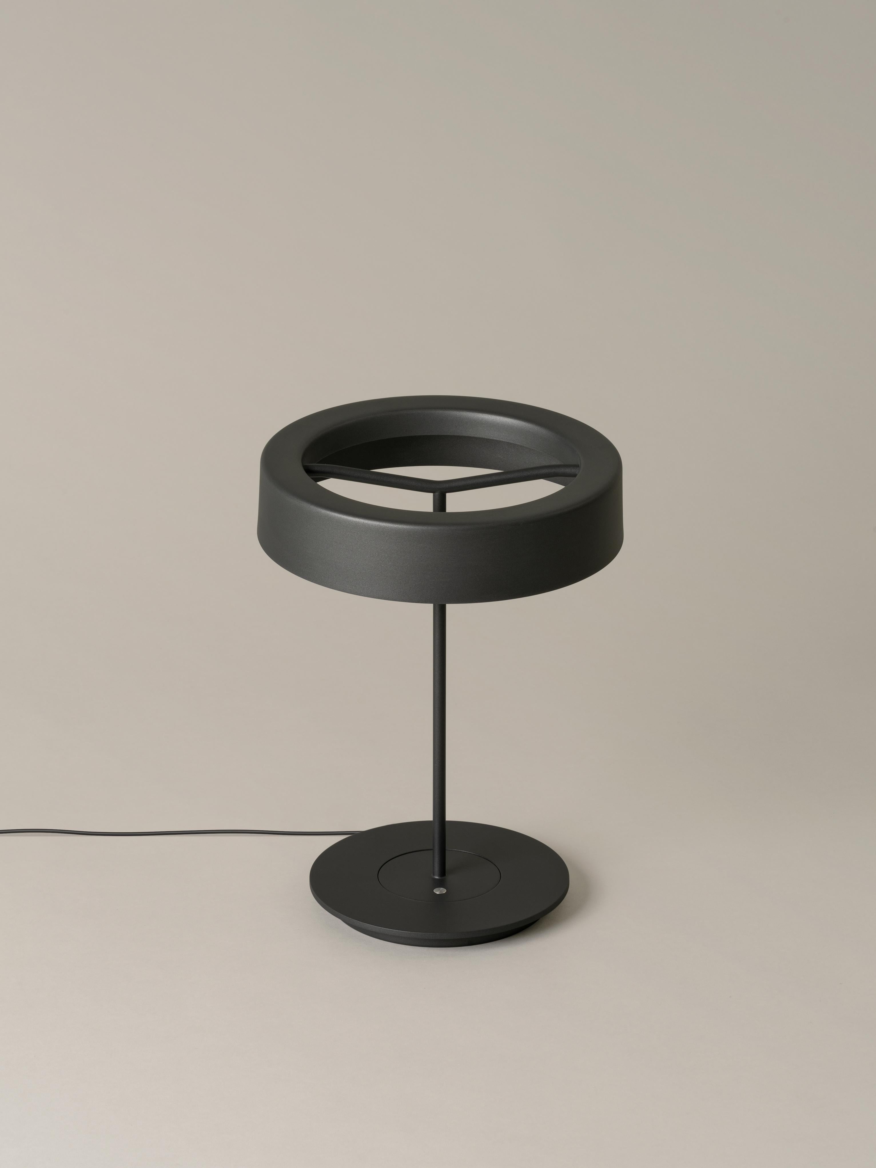 Small graphite sin table lamp with shade by Antoni Arola.
Dimensions: D 27 x H 36 cm.
Materials: Metal.
Available in white or graphite, with or without shade.

A lamp that combines simplicity and technology to create a lucent ring of light
