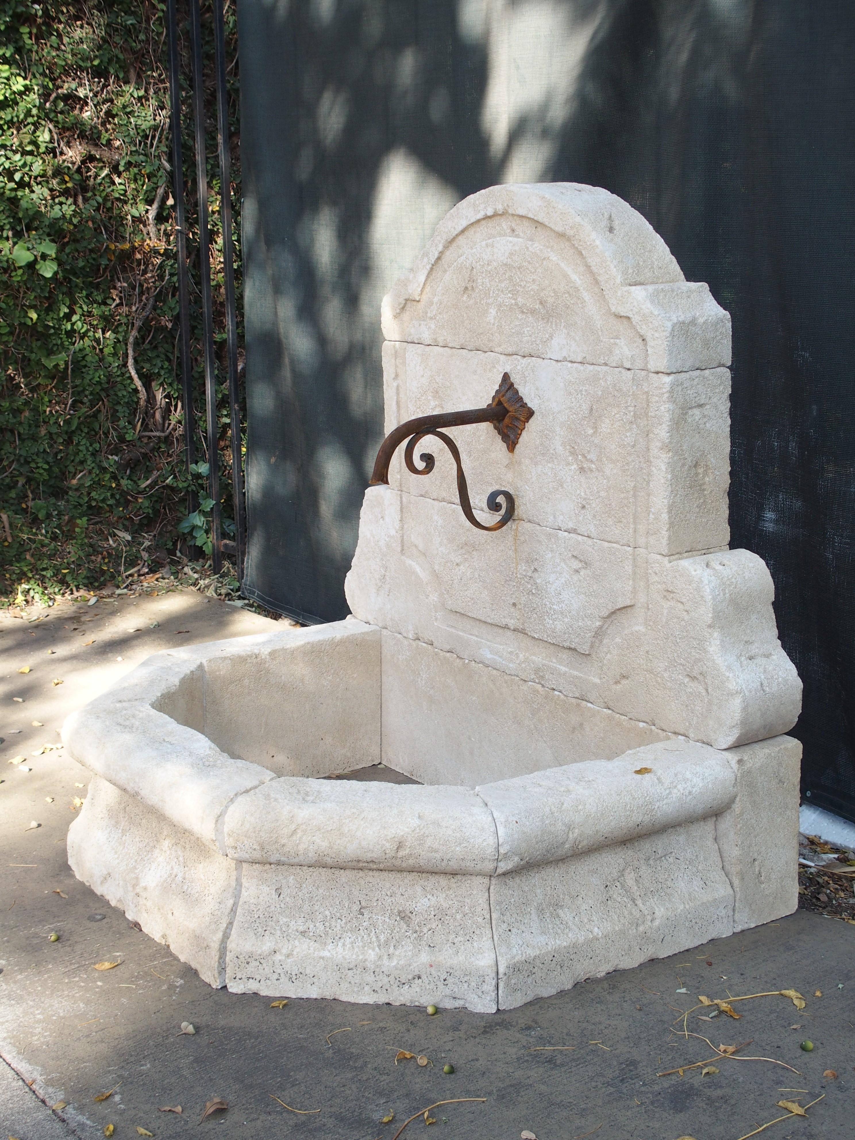 This elegant, small wall fountain from Provence has been hand carved in Estaillade limestone. The arched top has canted shoulders and is flanked by a pair of scroll-shaped corbels. The back wall appears to be raised due to an indentation which
