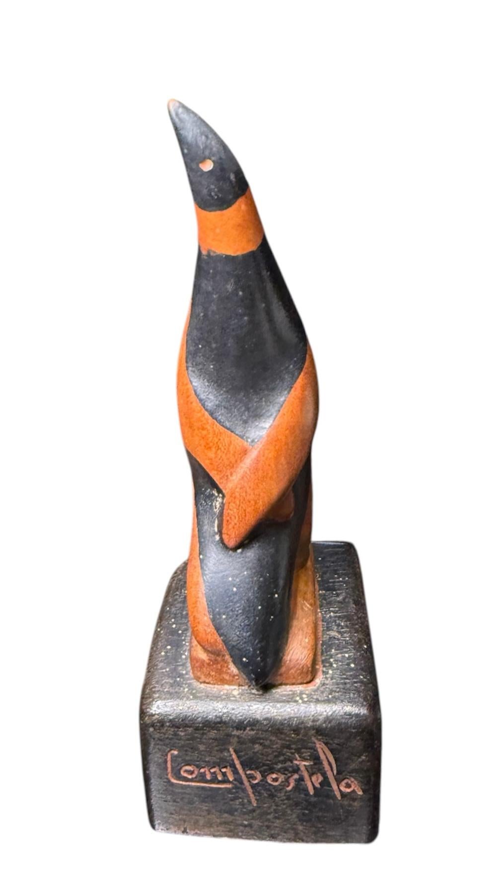 This is a Hand Carved Wood Penguin Sculpture. It depicts a black and orange color small penguin standing up and looking up. The bird sculpture is supported by a heavy cubic shaped wood base. In the center of the base is signed Compostela, the