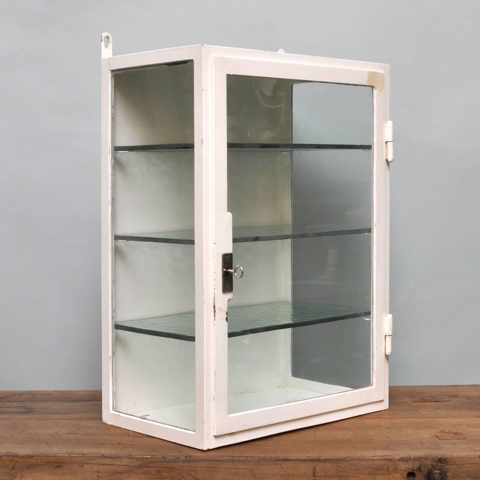 Small medicine cabinet, wall unit which originates from the 1940s. It is made from thick iron with the original antique glass and shelves. It features a good working lock and key system.