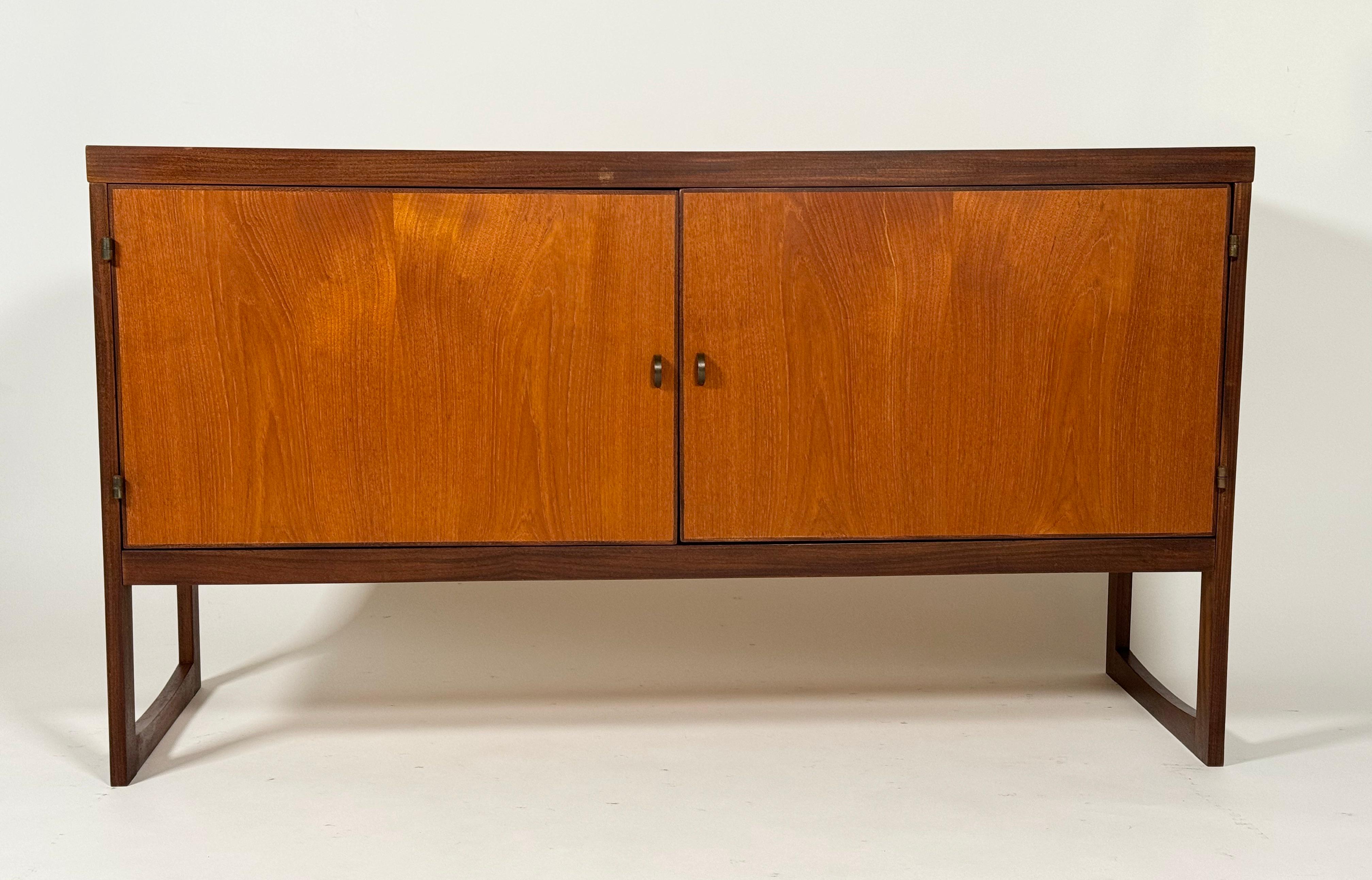 Compact Hans Olsen teak and birch sideboard with one adjustable with an birch lined interior. Curved brass hardware for the pulls and hinges. Having an angular form with squared off legs going into the body of the case good. The warmth of wood with