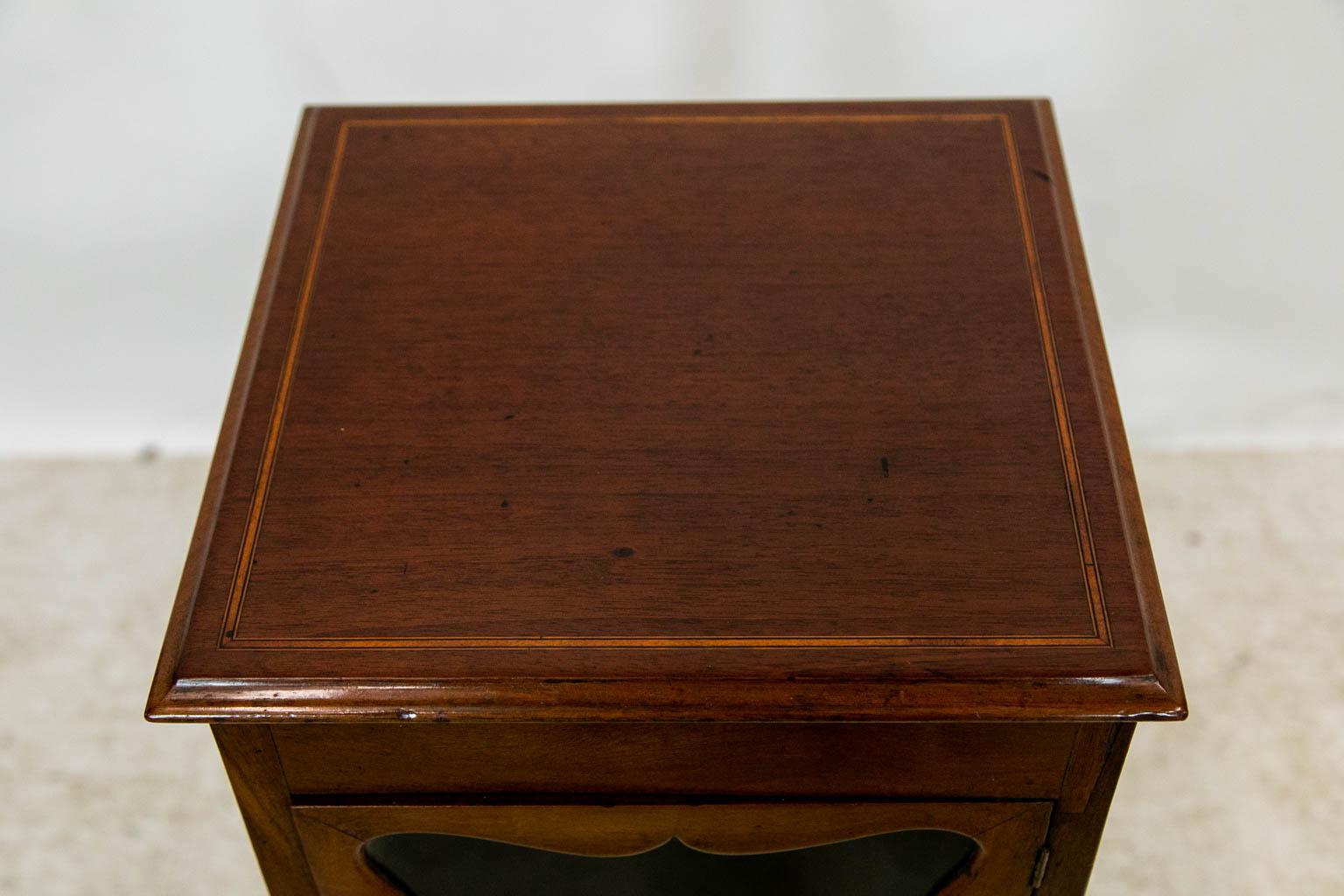 The top of this cabinet is inlaid with ebony and boxwood banding. The cabinet section has glass windows on all four sides that have shaped framing. The single drawer below the cabinet is inlaid with boxwood stringing. The four legs are connected