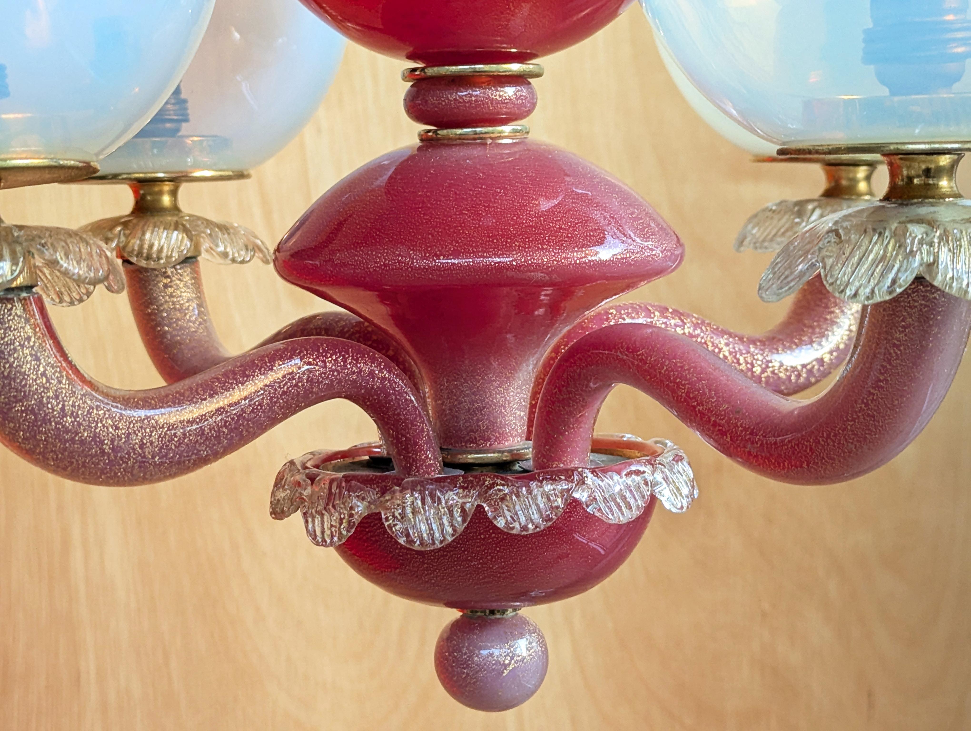 Questo bellissimo ed elegante lampadario a 4 luci è stato realizzato a Murano, in Italia, intorno agli anni Cinquanta. È realizzato a mano in vetro in un colore trasparente, cremisi e iridescente. 
Le parti in vetro trasparente e cremisi presentano