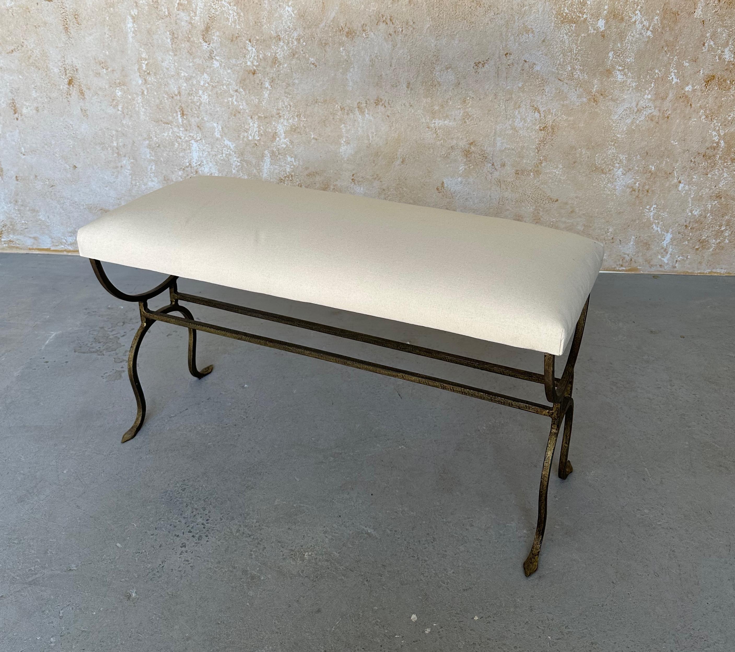 An elegant small scale bench made of forge iron with a hand applied burnished gilt finish. The seat is currently in muslin and it is ready to be upholstered. 