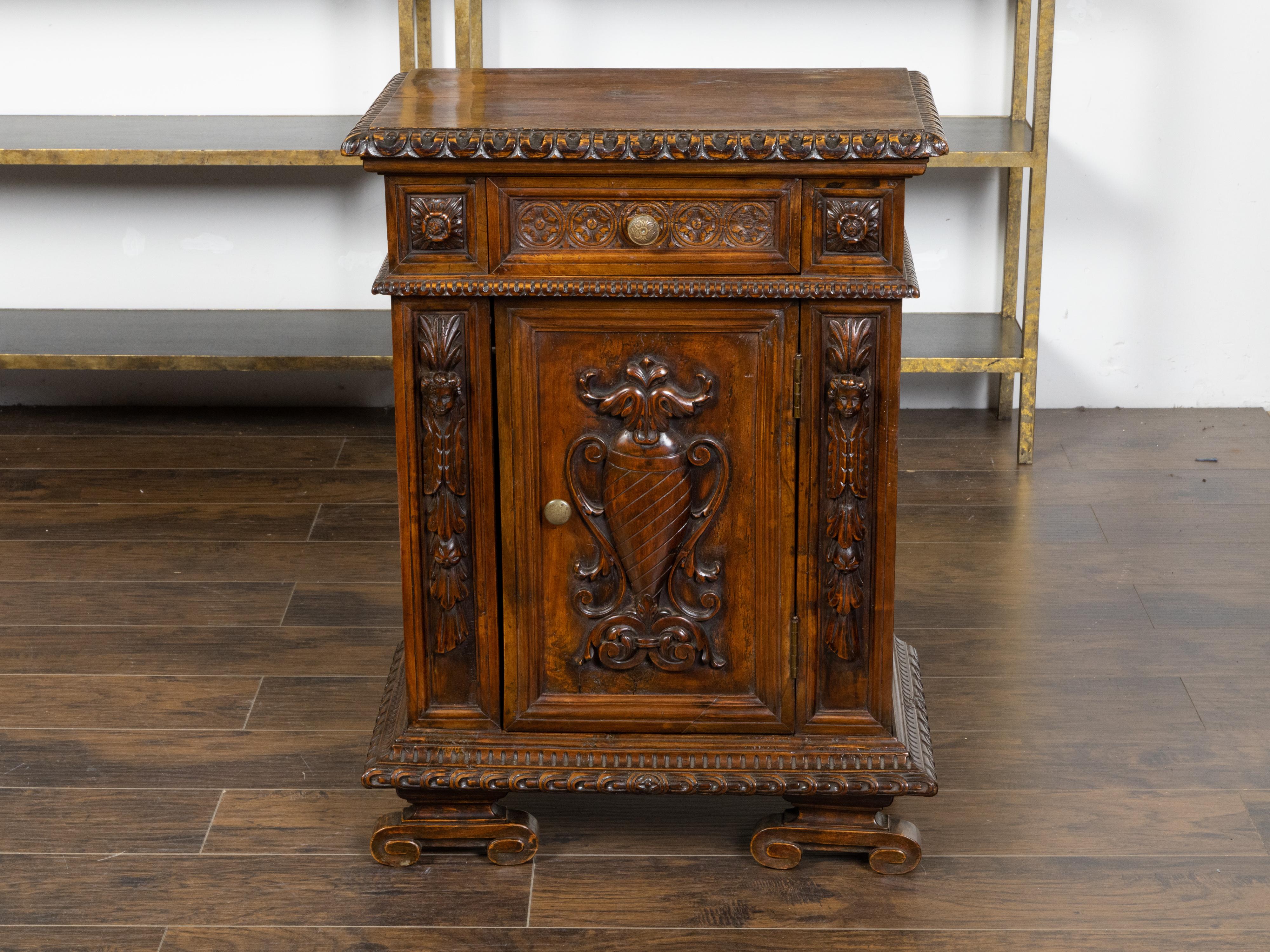 An Italian walnut small cabinet from the early 19th century, with single drawer over single door, carved foliage, vase and mascaron motifs. Created in Italy during the early years of the 19th century, this walnut cabinet features a rectangular top