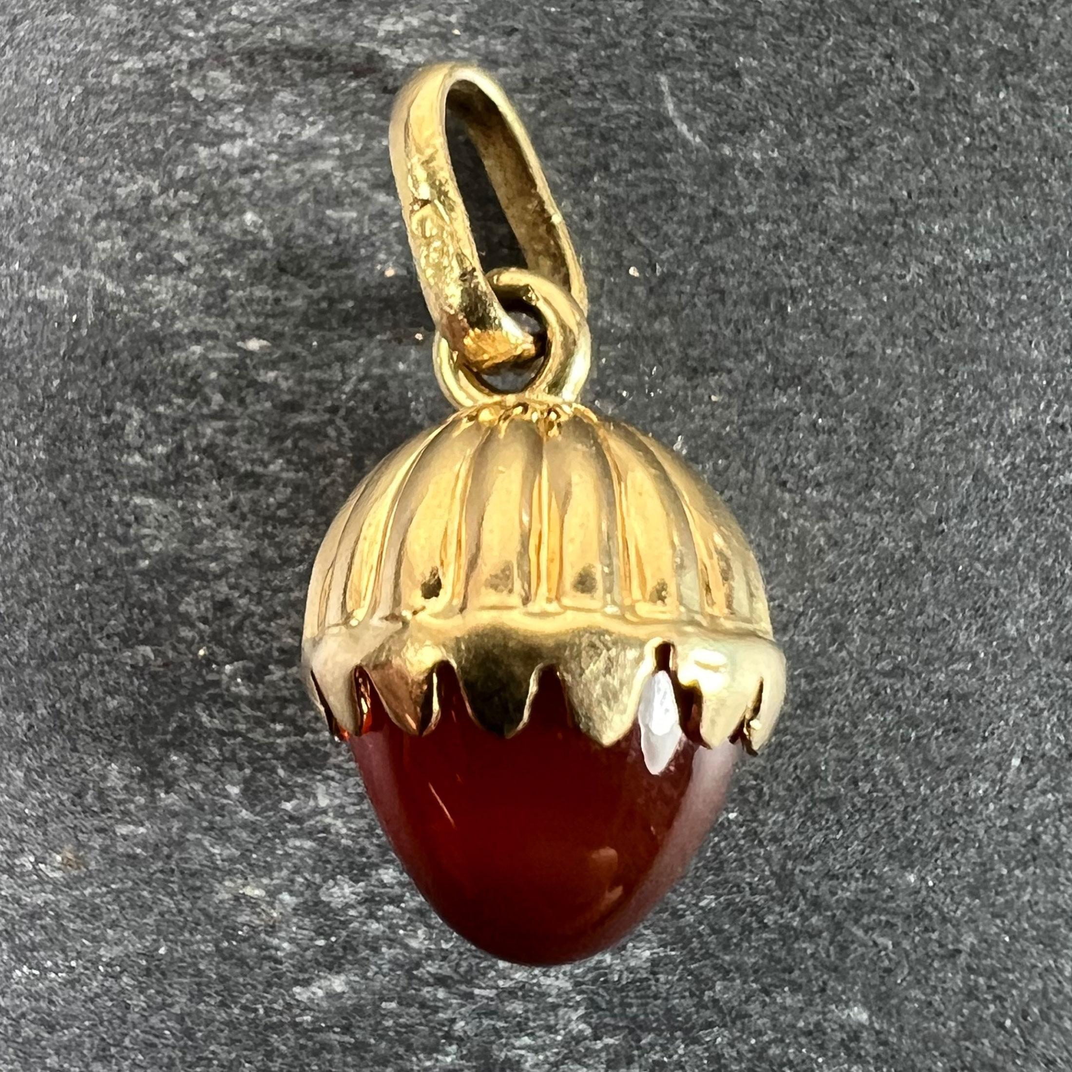 Pendentif à charme en or jaune 18 carats (18K) conçu comme un gland avec une noix en calcédoine orange (cornaline) sculptée et un sommet en or strié. Les glands symbolisent la fertilité, la croissance, les nouveaux départs et le potentiel.