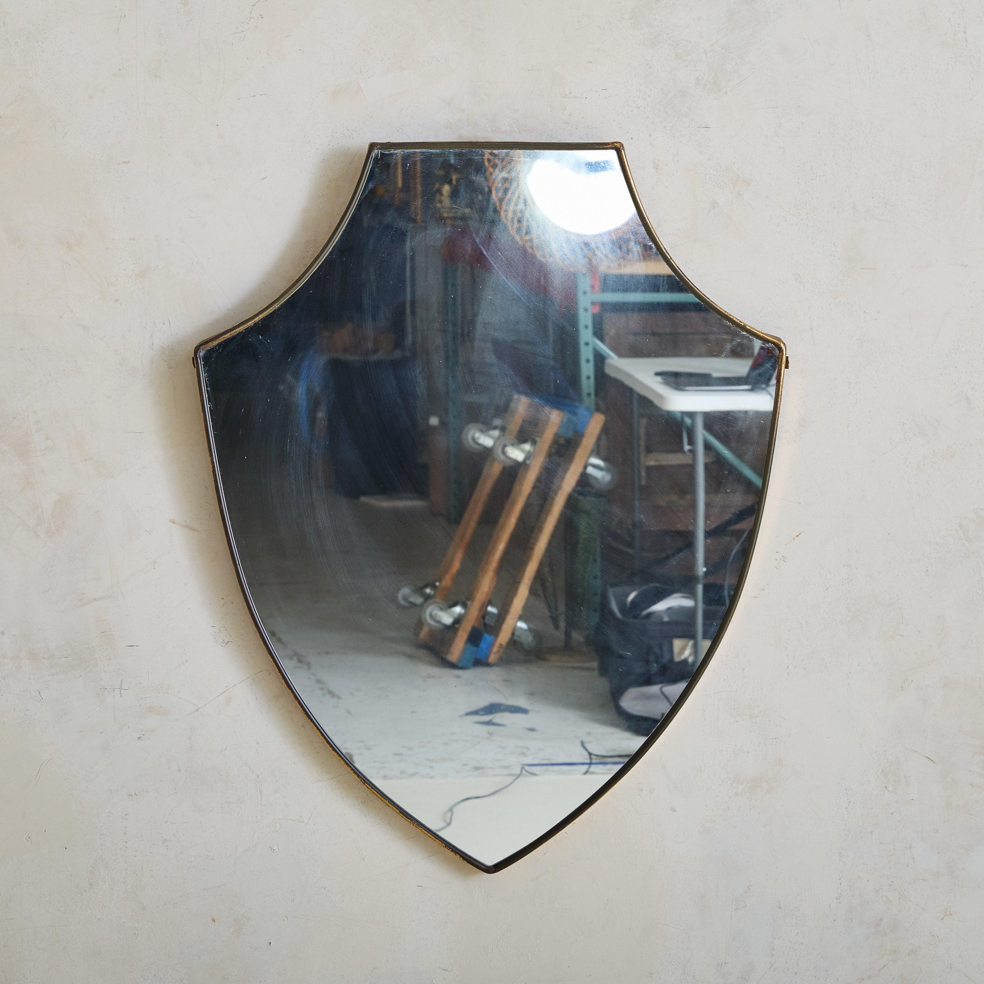 Specchio da parete italiano a forma di scudo degli anni '70, caratterizzato da due eleganti curve lungo la parte superiore e da una silhouette affusolata. Questo specchio ha una delicata cornice in ottone con una bellissima patina invecchiata. Un