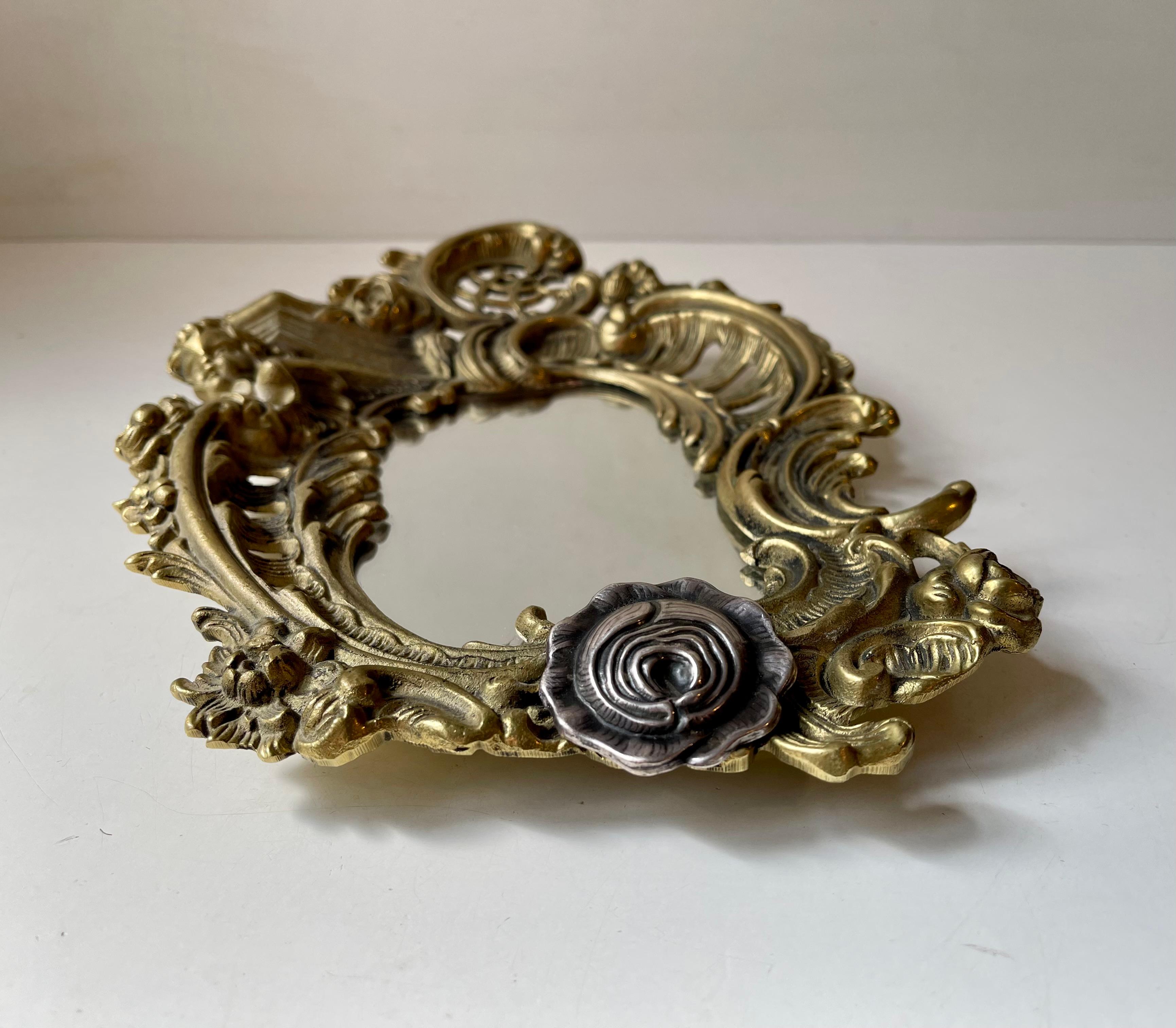 Ornate cast and partially perforated brass mirror decorated with leaves, flowers, an angel and a rosetta in sterling silver. It was made in Italy, probably/possibly bespoke, during the 1970s after neoclassical derived ideals. Measurements: 28x20x5