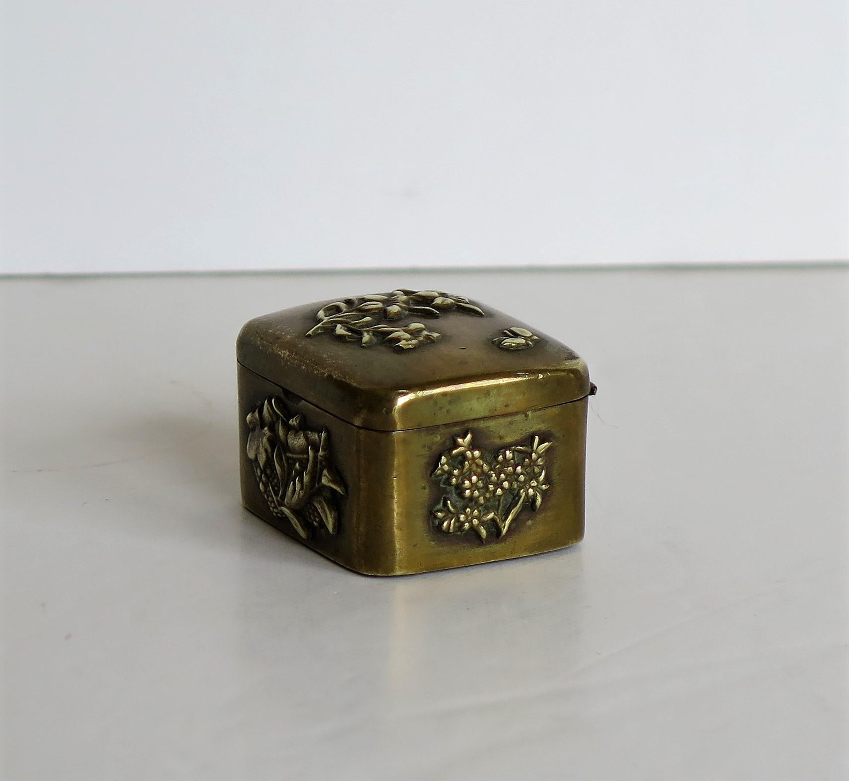 This is a small Japanese bronze and brass box with a hinged lid and different detailed embossed applied patterns of flowers and leaves, dating to the 19th century Meiji period.

The box has a rectangular shape with a hinged slightly domed top