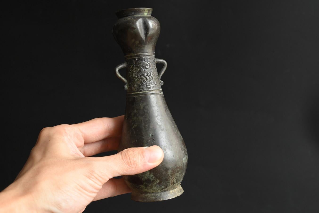 This is a copper vase made around the late Edo period.
The body is cast.
This is a vase for holding flowers to be offered in a tokonoma alcove or in front of a Buddha.
The tip is shaped like a flower bud, and the bottom expresses a wave pattern.
It