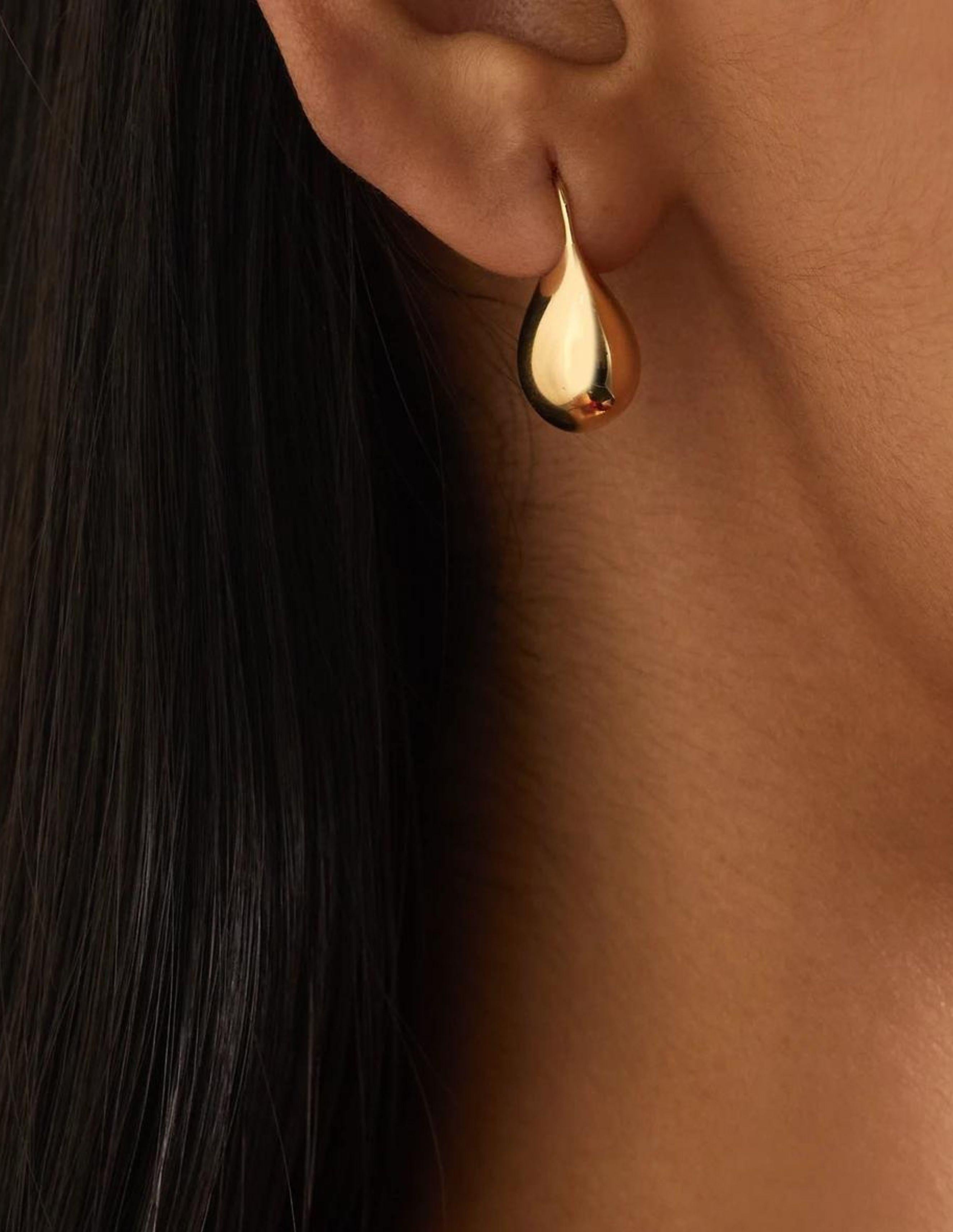 18K Gold drop earrings inspired by the shapes of water jugs and calf skin sacs, the objects that hold what we need for the journey. A vision of unspillable life. Polished and minimal with sculptural allure. 0.75 inch drop on hook fastening for