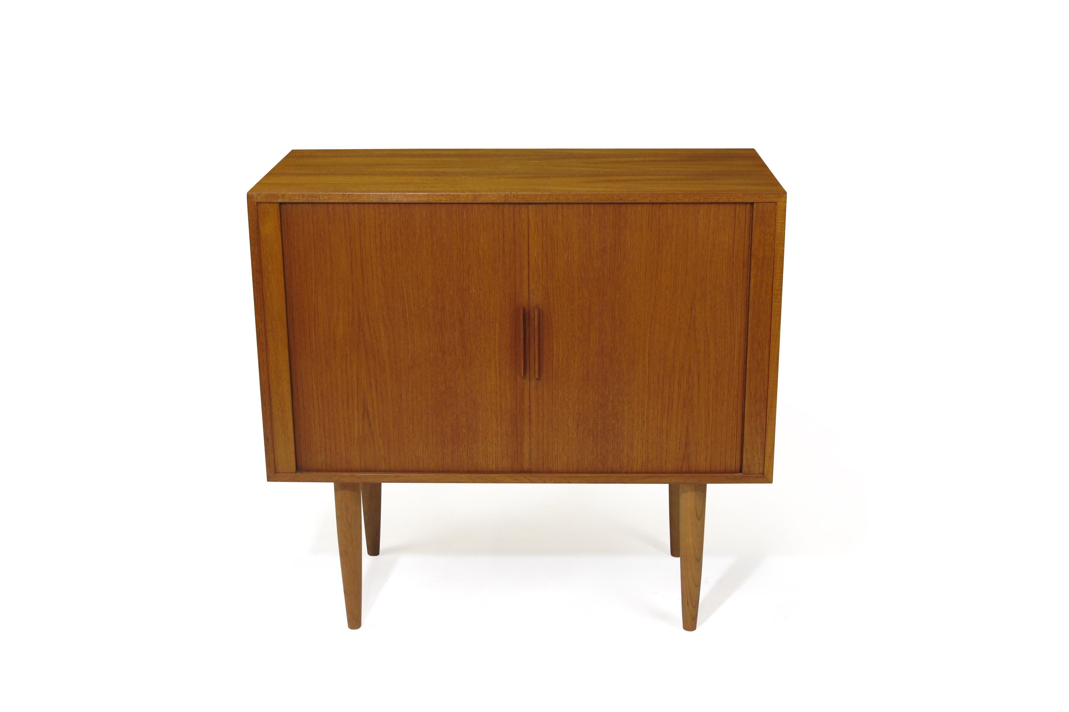 Midcentury Teak cabinet designed by Kai Kristiansen for the FM System. Cabinet features dual tambour doors, adjustable interior shelf, and single drawer with teal base. Minimal design with mitered edges and raised on 12