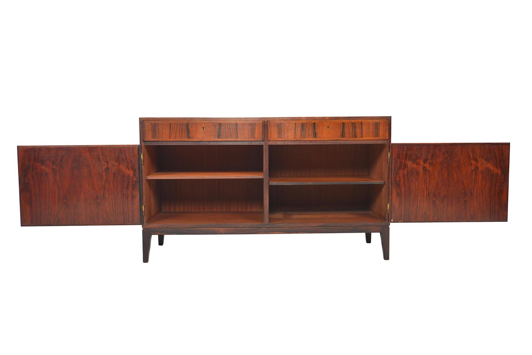 This beautiful credenza was designed by Kai Winding in the 1960s. Flush cabinet drawers and doors showcase beautiful rosewood grain patterning. Cabinet offers two bays with adjustable shelving. Piece includes original locking key. In excellent