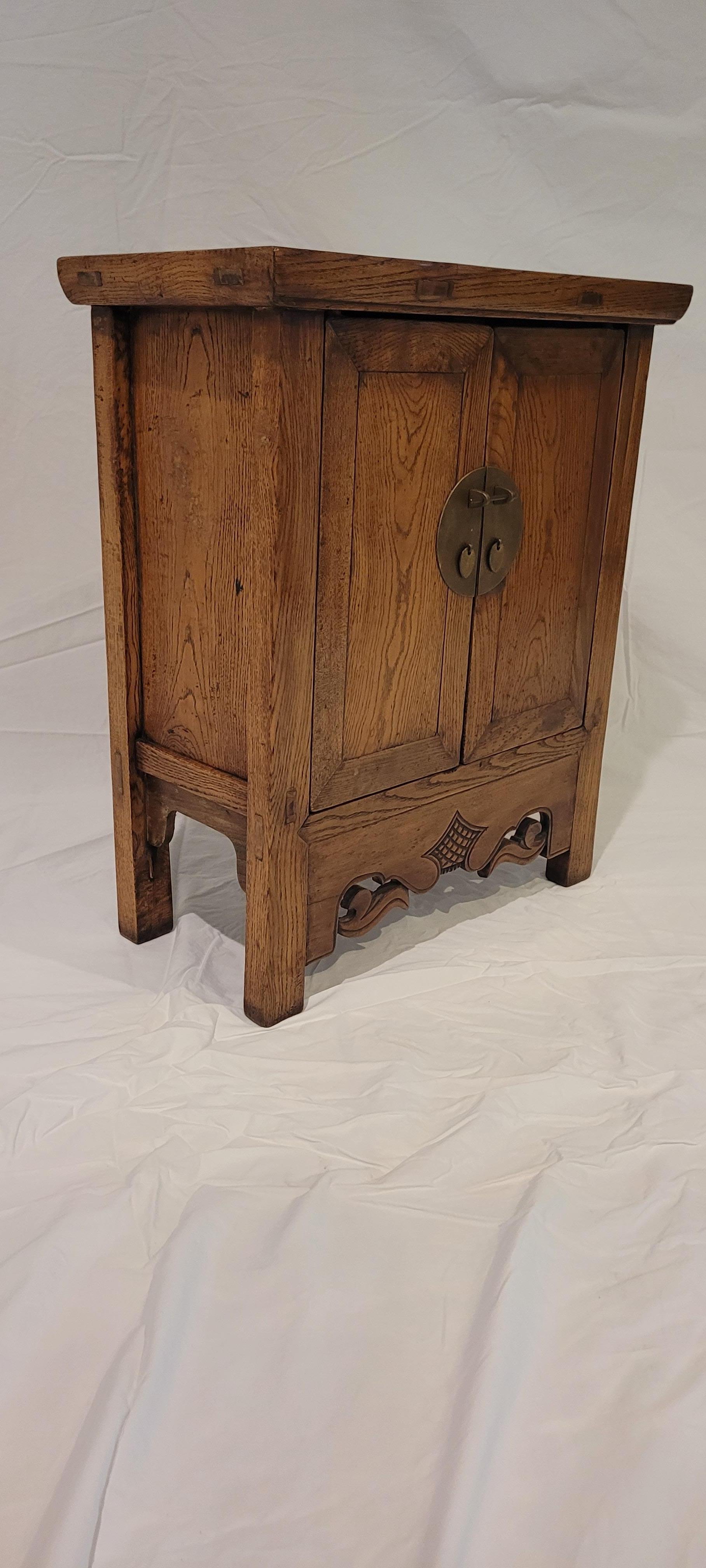 Small Kang Cabinet	22.25h x 18.5w x 9.75d
This small kang cabinet has a slight tapered form.  The aprons are done in open carved style carvings.  The metal on the front is round.  The frame of the top is mitered with mortised and tenoned members. 