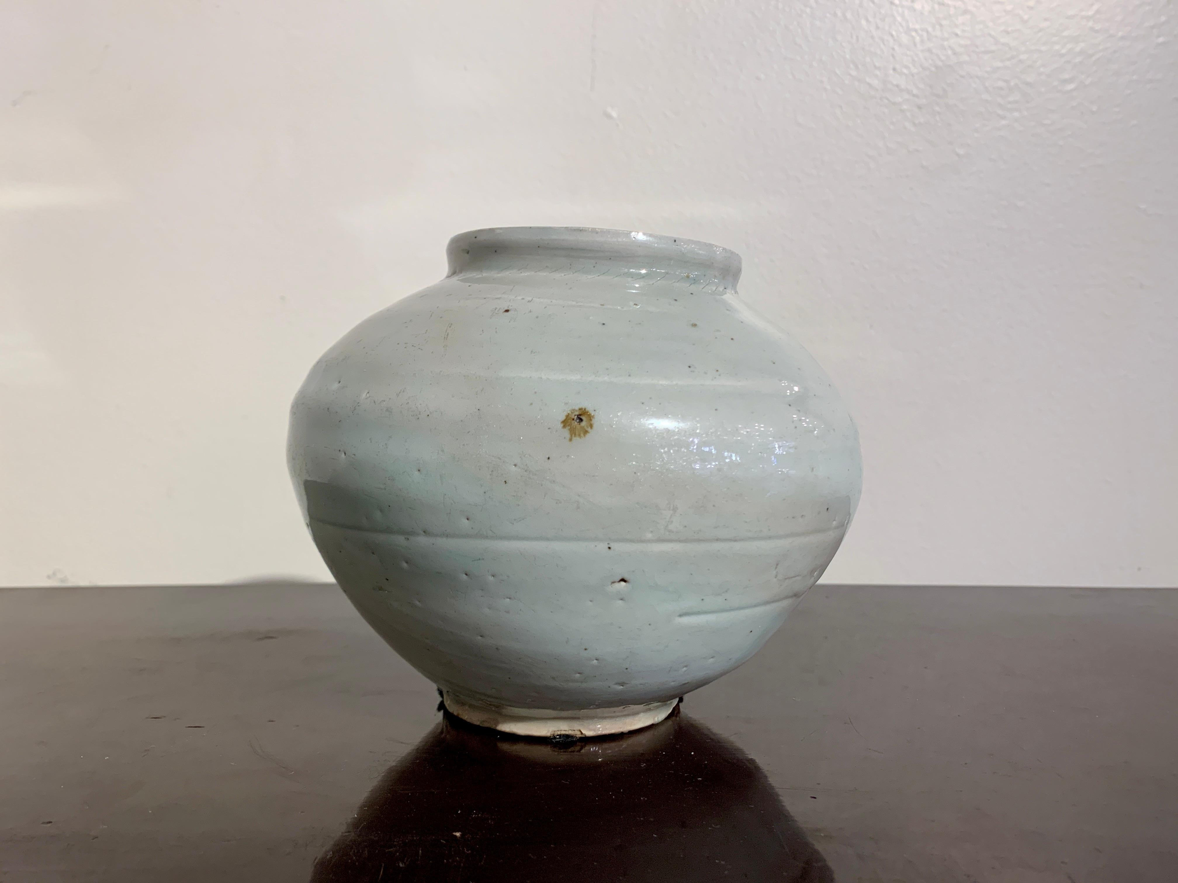 A subtle and sublime small Korean white glazed porcelain moon jar, Joseon Dynasty, 18th/19th century, Korea.

The small moon jar of typical form, with a slightly irregular globular body set upon a short ring foot. The high sloped shoulders support