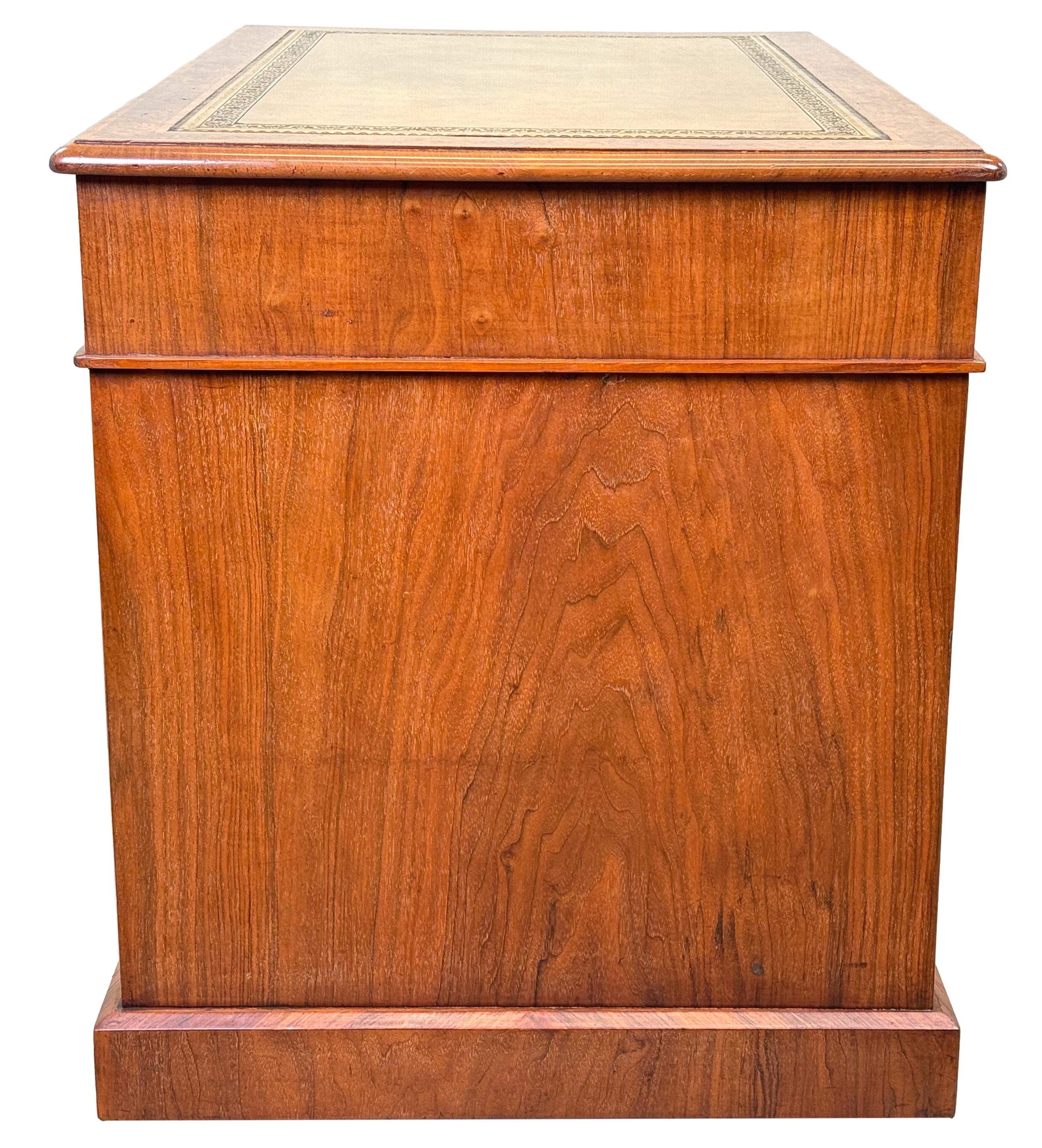 Una splendida scrivania a piedistallo in radica di noce della fine del XIX secolo, di piccole e rare proporzioni, con un attraente inserto in pelle lavorata sul piano a fasce incrociate, sopra nove cassetti di grande figura, con decorazioni a fasce