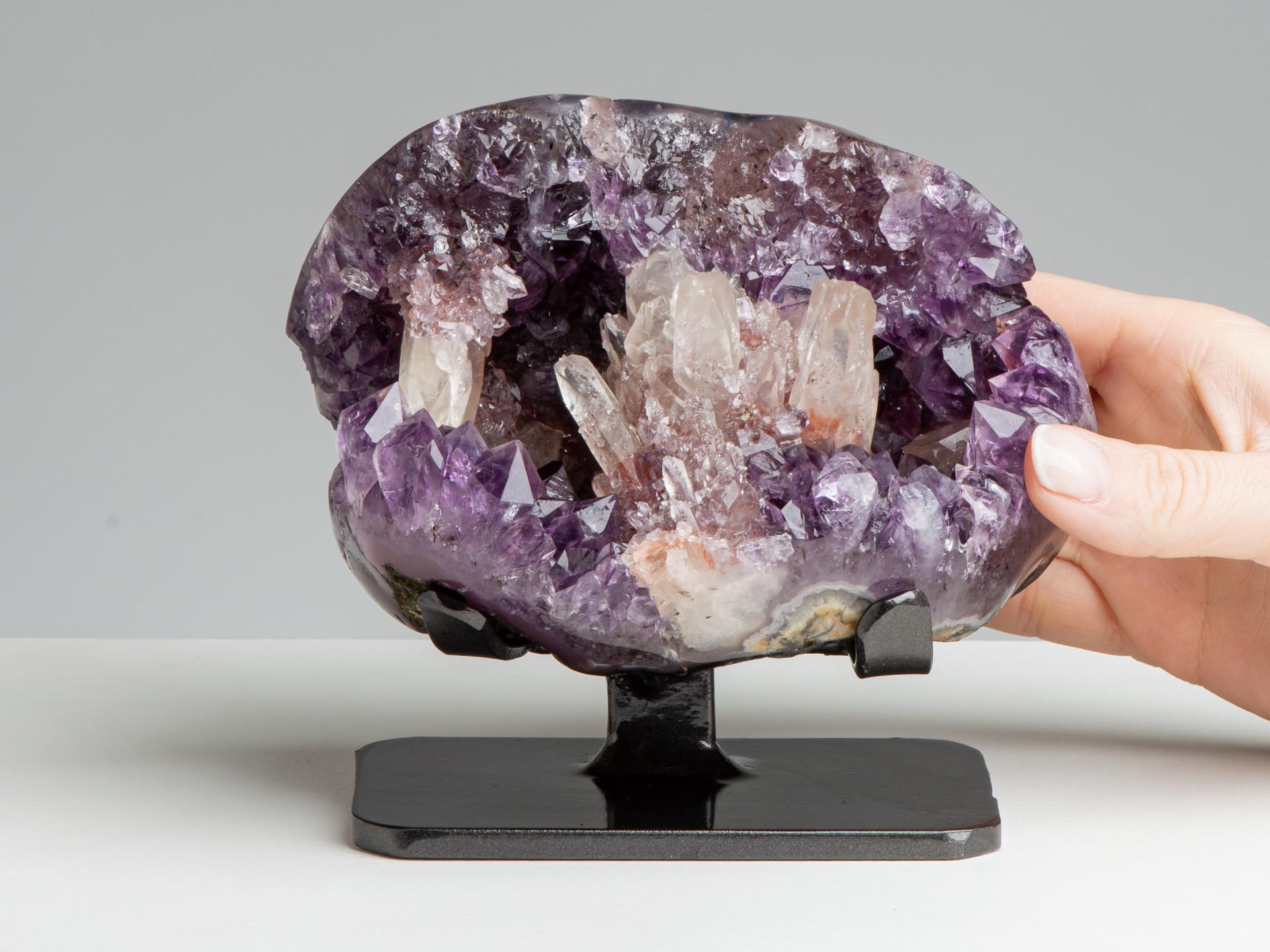 This small geode of lilac coloured amethystine quartz with several rhombohedral
calcites at the front and red druze / blackish goethite accents.

This piece was legally and ethically sourced directly in the prestigious mines of Uruguay, South