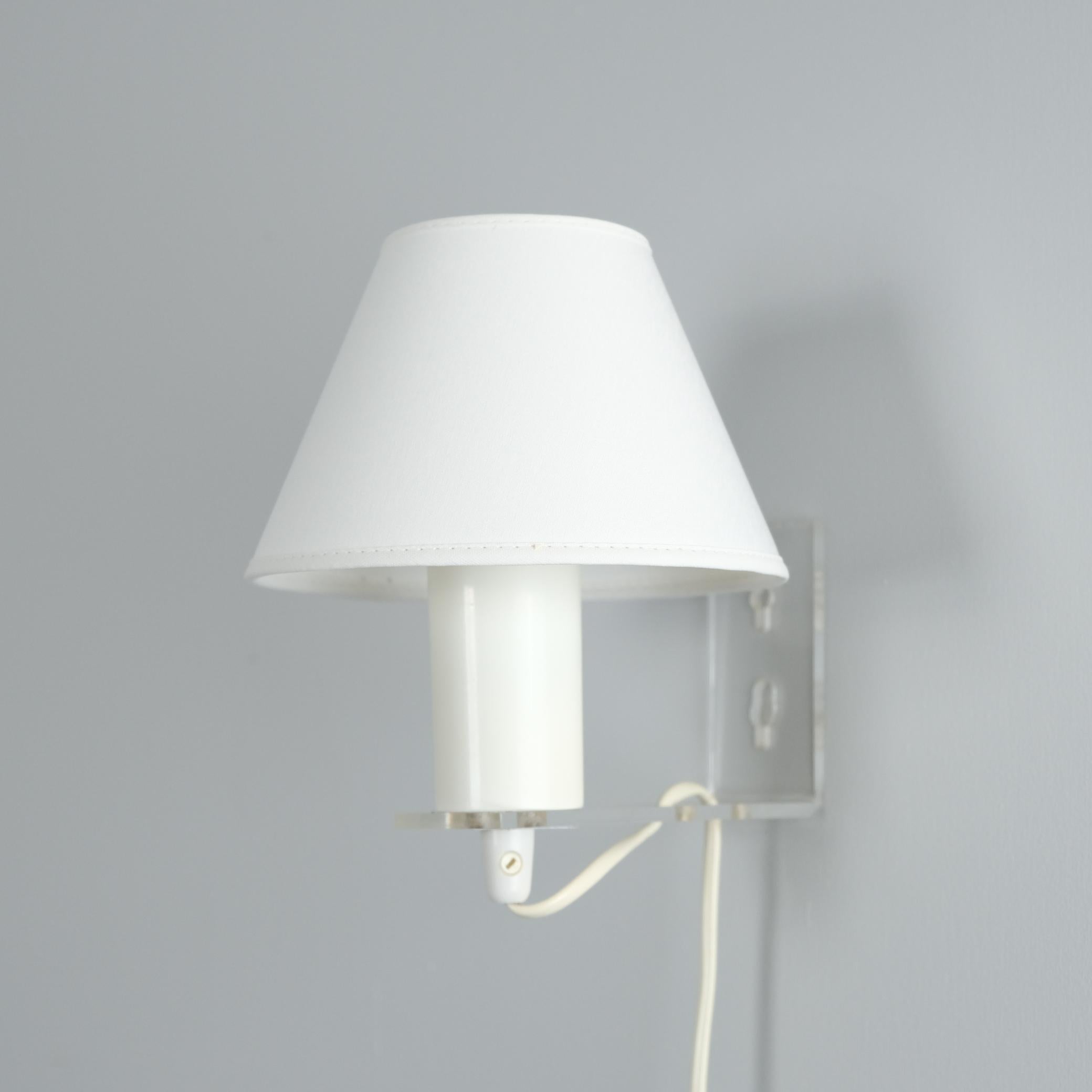 Eine niedliche Bijou-Wandleuchte von Lisa Johansson-Papé für Orno-Stockmann. Die Leuchte besticht durch ihr minimalistisches Design mit einem L-förmig gebogenen Acrylarm in klarer Farbe, der die Leichtigkeit der Leuchte noch verstärkt. Der weiße