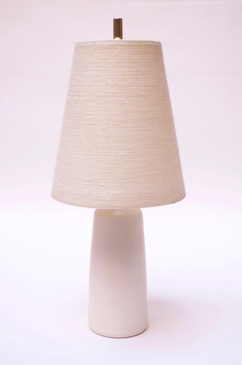 This small scale table lamp was designed and manufactured in the 1960s by Lotte and Gunnar Bostlund after they relocated their ceramic studio from Denmark to Canada. Includes original Lotte jute shade The applied, unpolished brass neck with warm