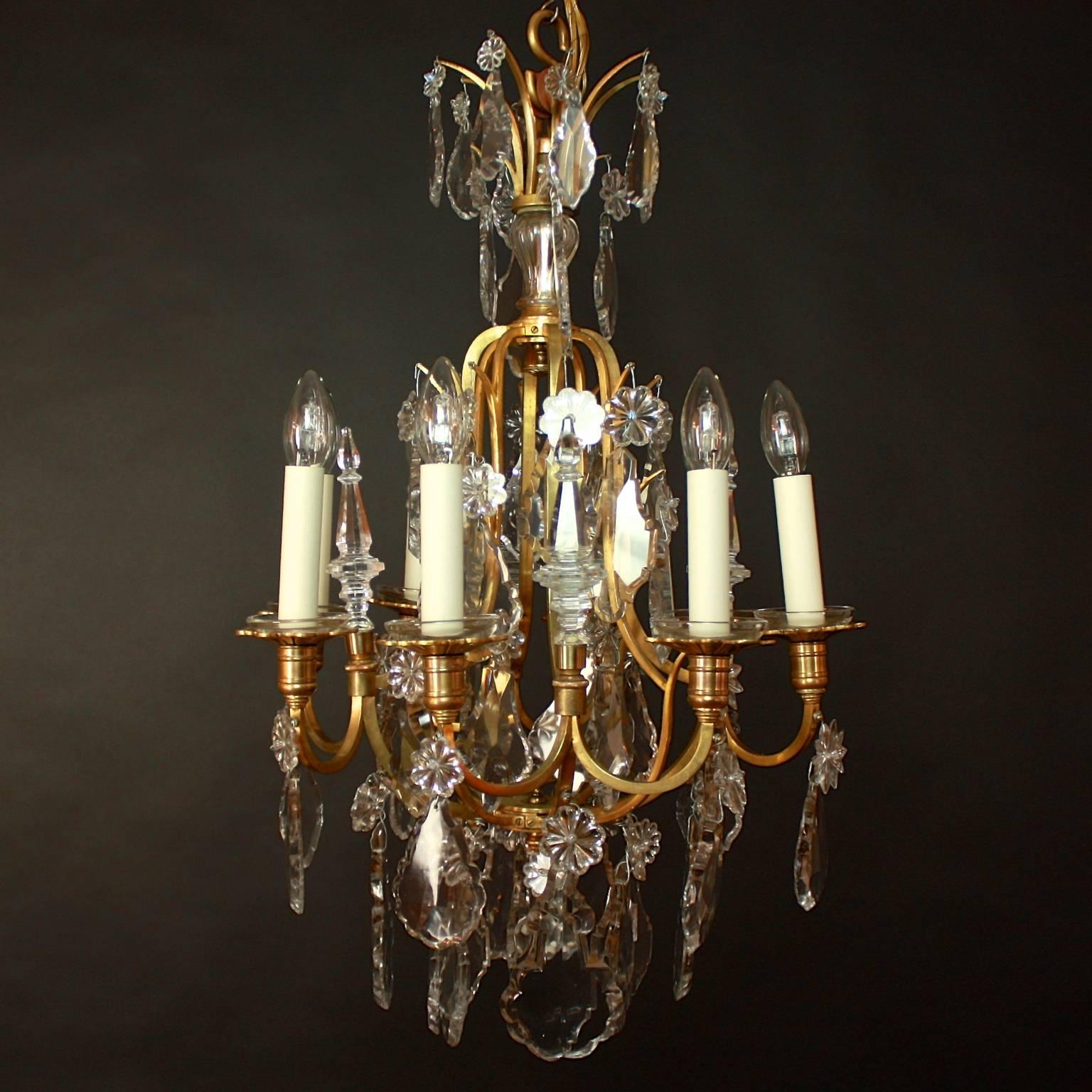 Exquisite Louis XV Style gilt bronze chandelier decorated overall in scalloped cut crystal pendalogues with stellar jewels and moulded baluster pinnacles. The open square gauge frame supports eight square scrolling arms with foliated drip pans.