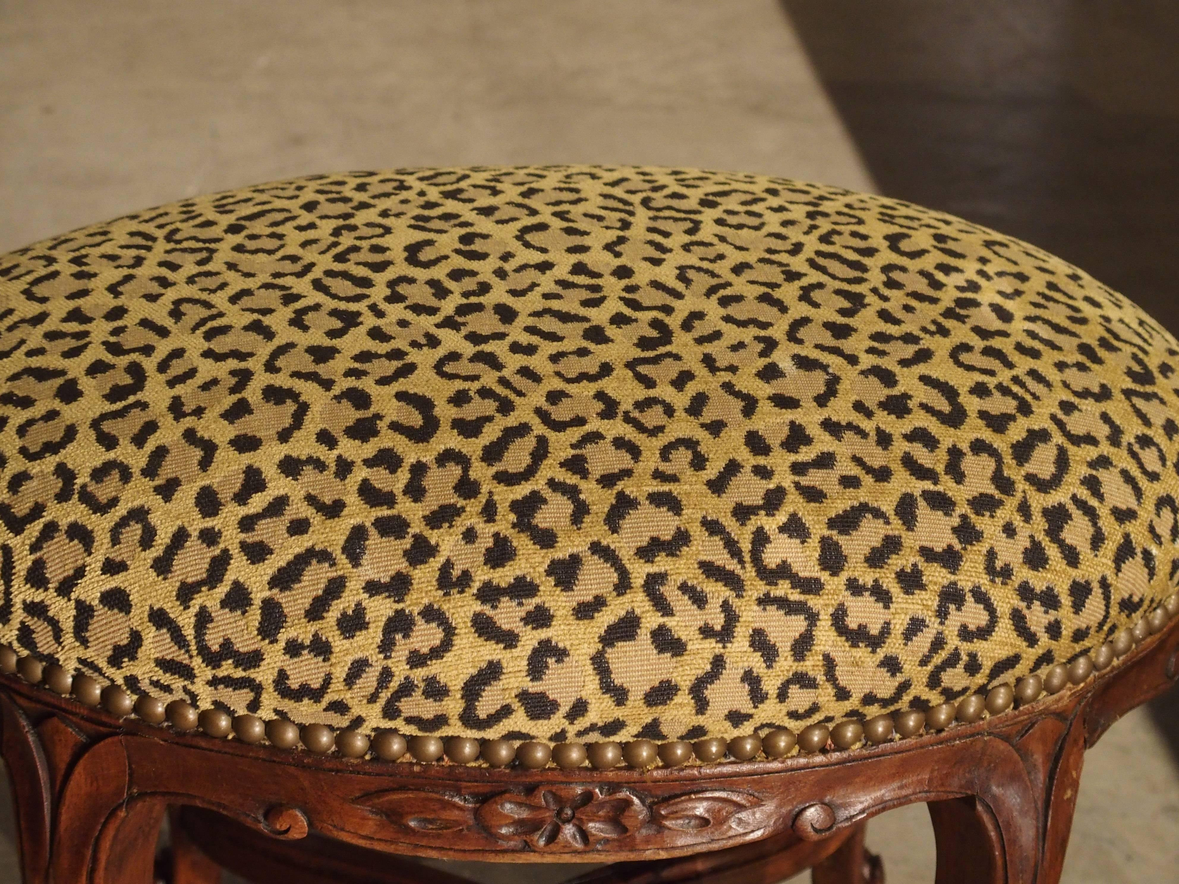 This early 1900s French foot stool from France is in the Louis XV style. Its shaped apron of S-Scrolls and C-Scrolls has foliate and floral motifs with stylized lily drops on the shoulders of the legs. The four scrolled feet are connected with